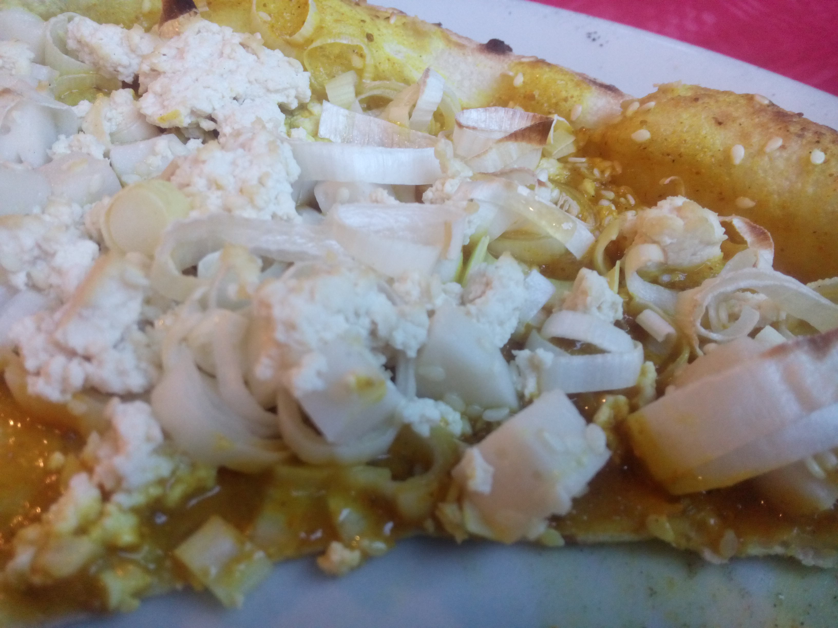 A close up of pizza with curry sauce and tofu