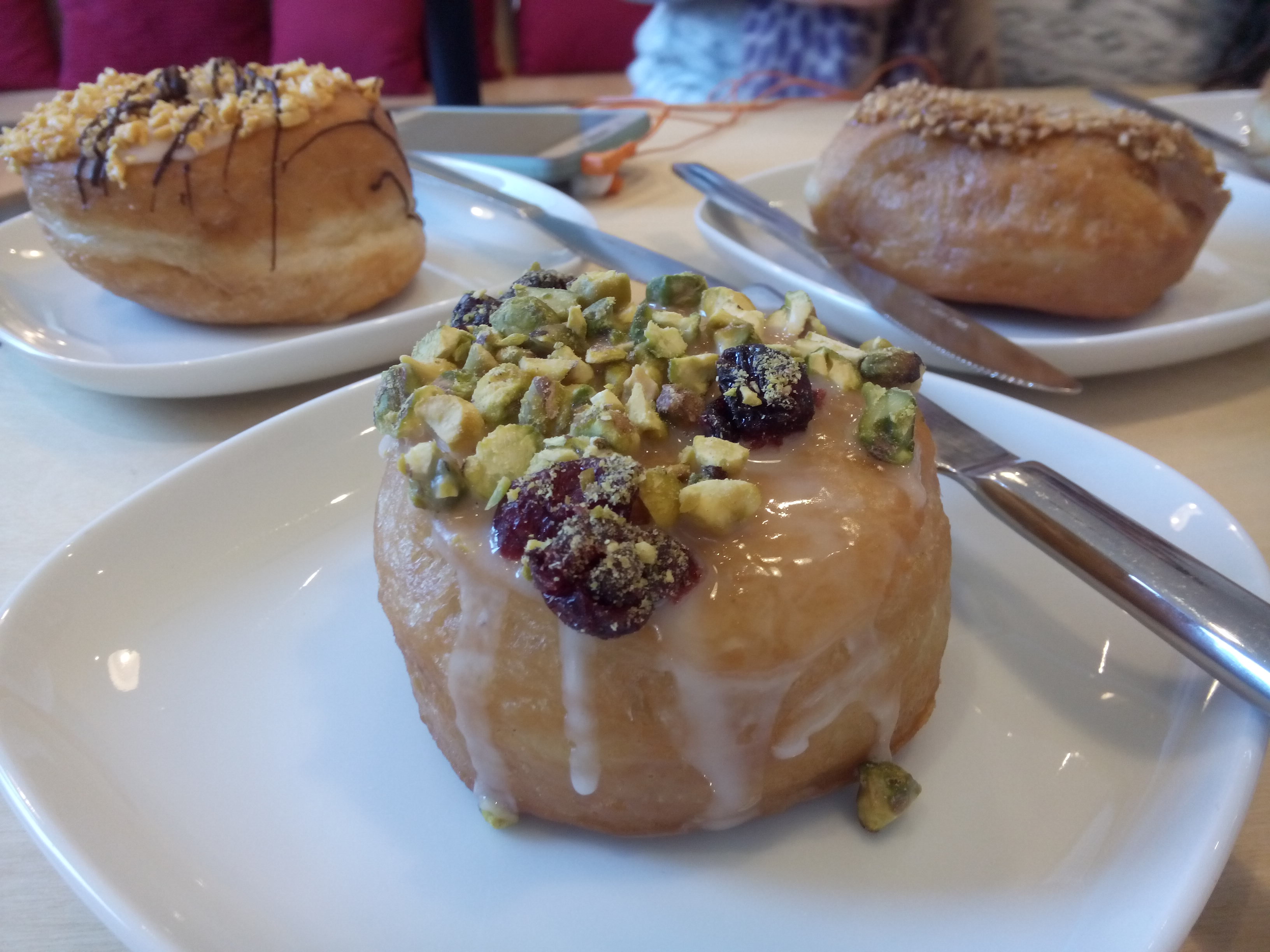 Three doughnuts on white plates; pistachio and cranberry in the foreground