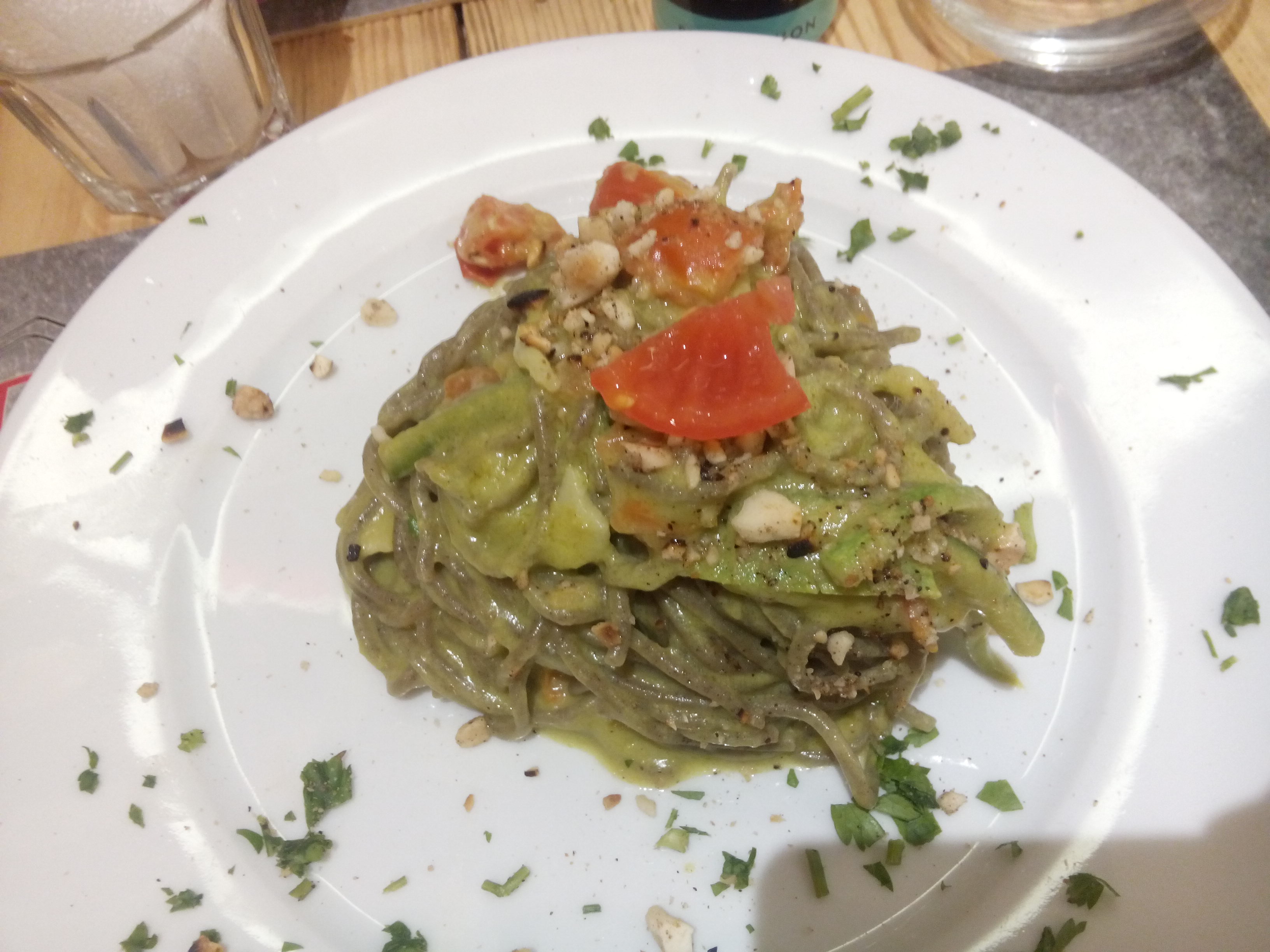 A white plate with a mount of green pasta and tomato on top