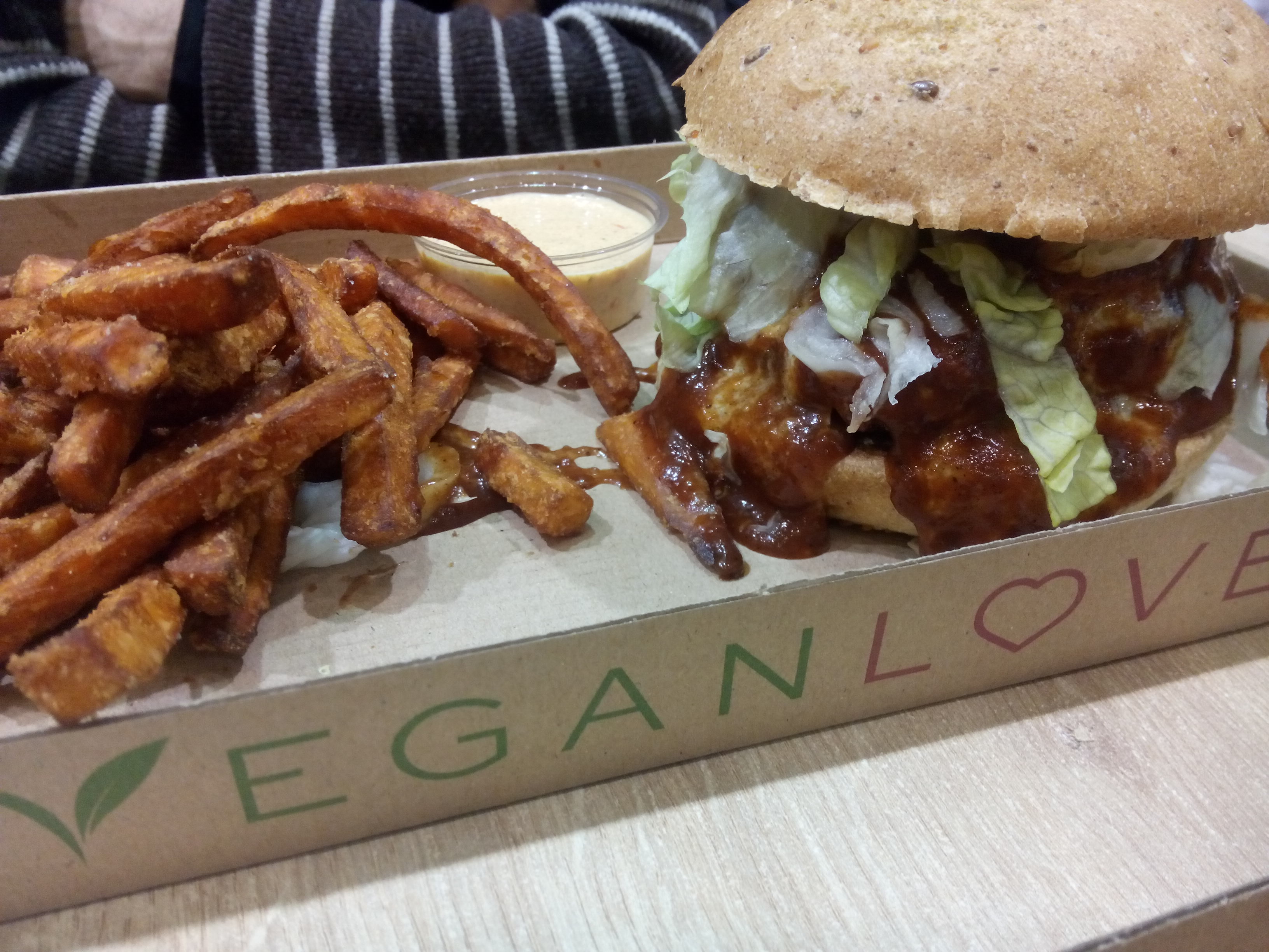 Sweet potatoe fries on one side of a cardboard tray and a sticky saucy salad-filled burger bun on the other