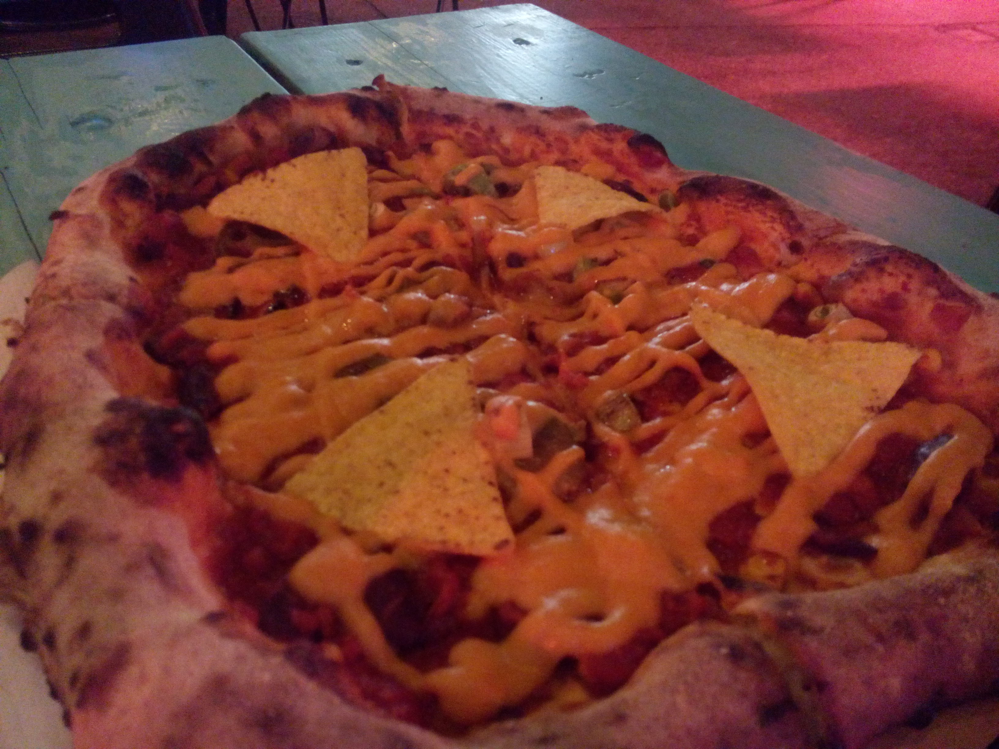 Dimly lit pizza with nachos and cheesey sauce on top