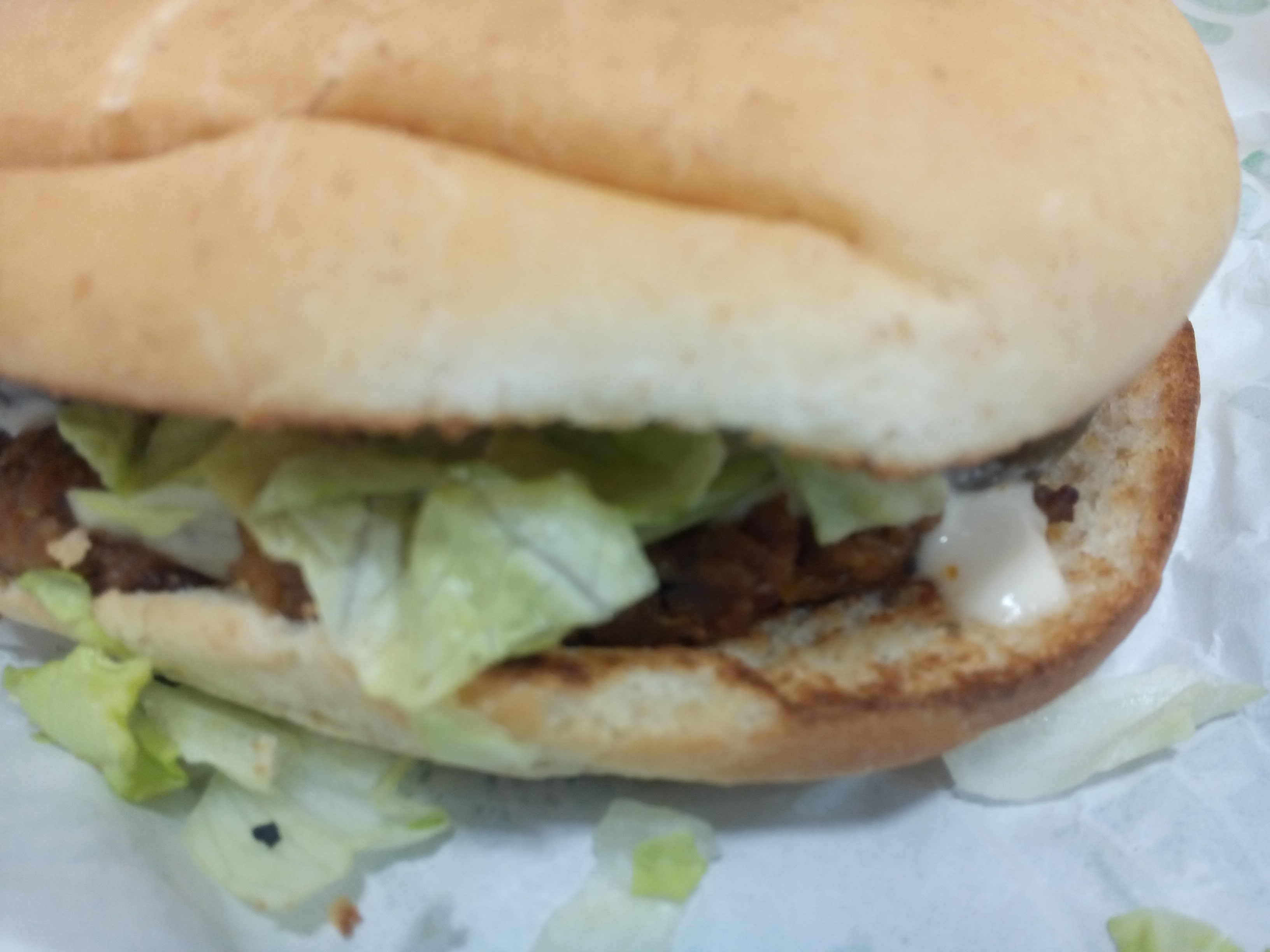 Close up of a bland looking burger bun with lettuce, sauce, and a bit of burger poking out