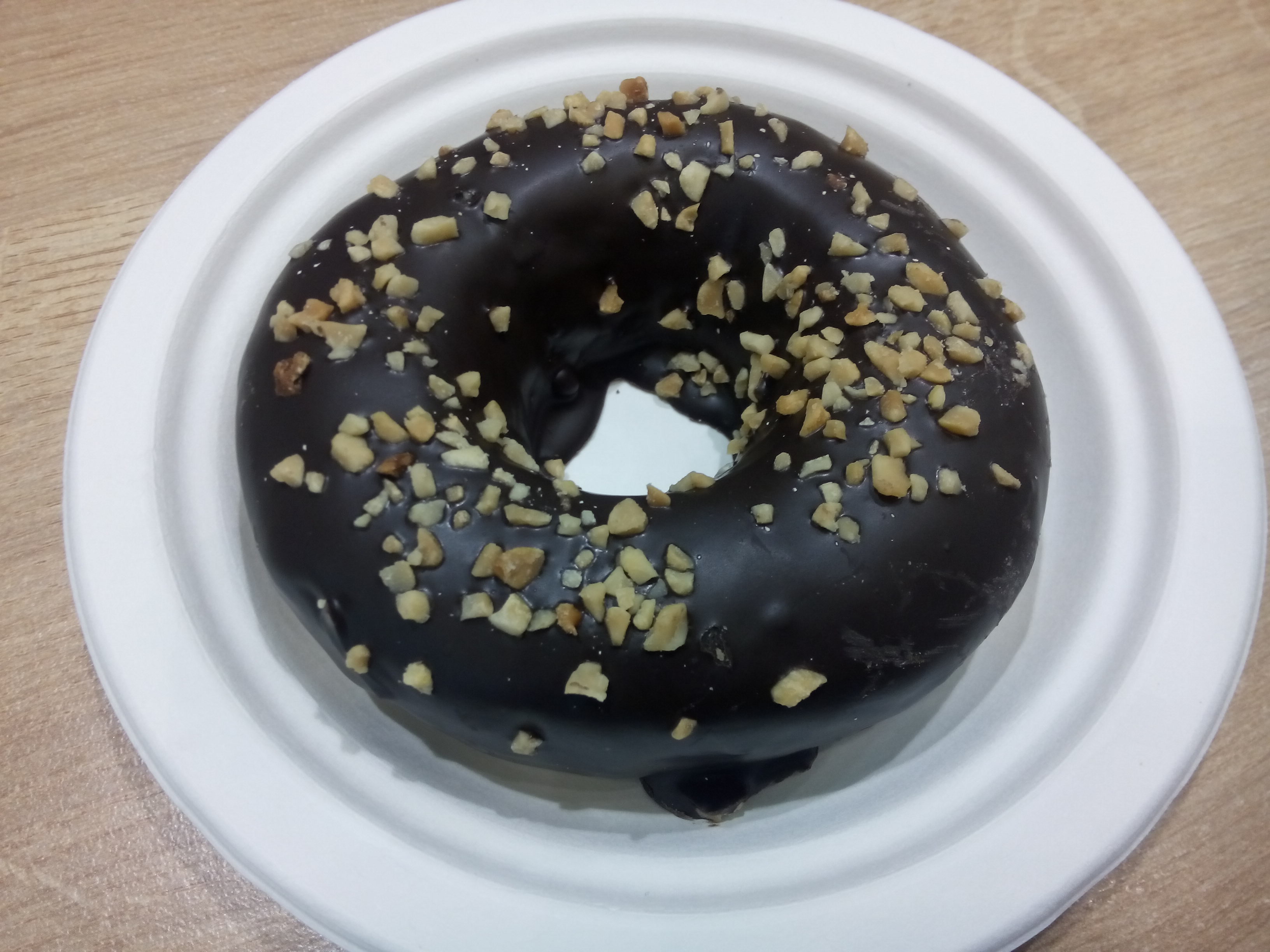 A white paper plate with a choclate and nut covered donut with a hole