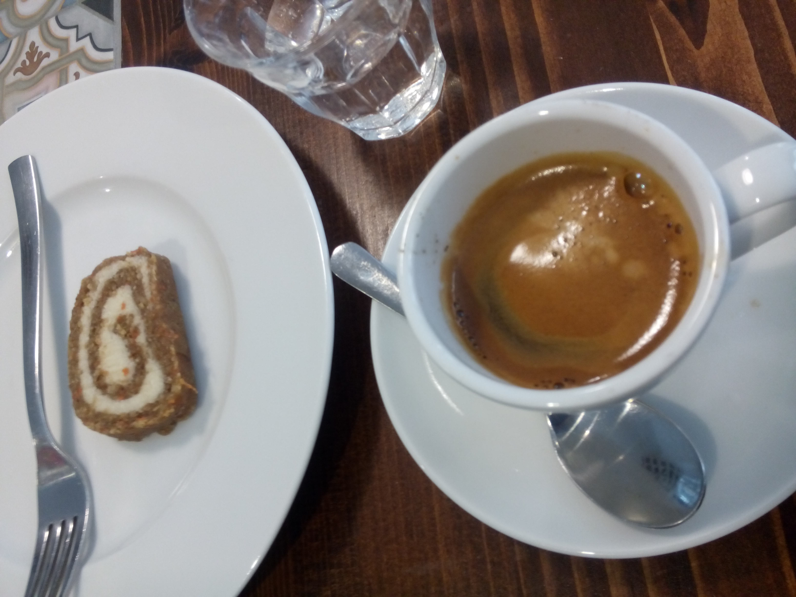 A small spiral cake on a plate with a fork beside a cup of coffee