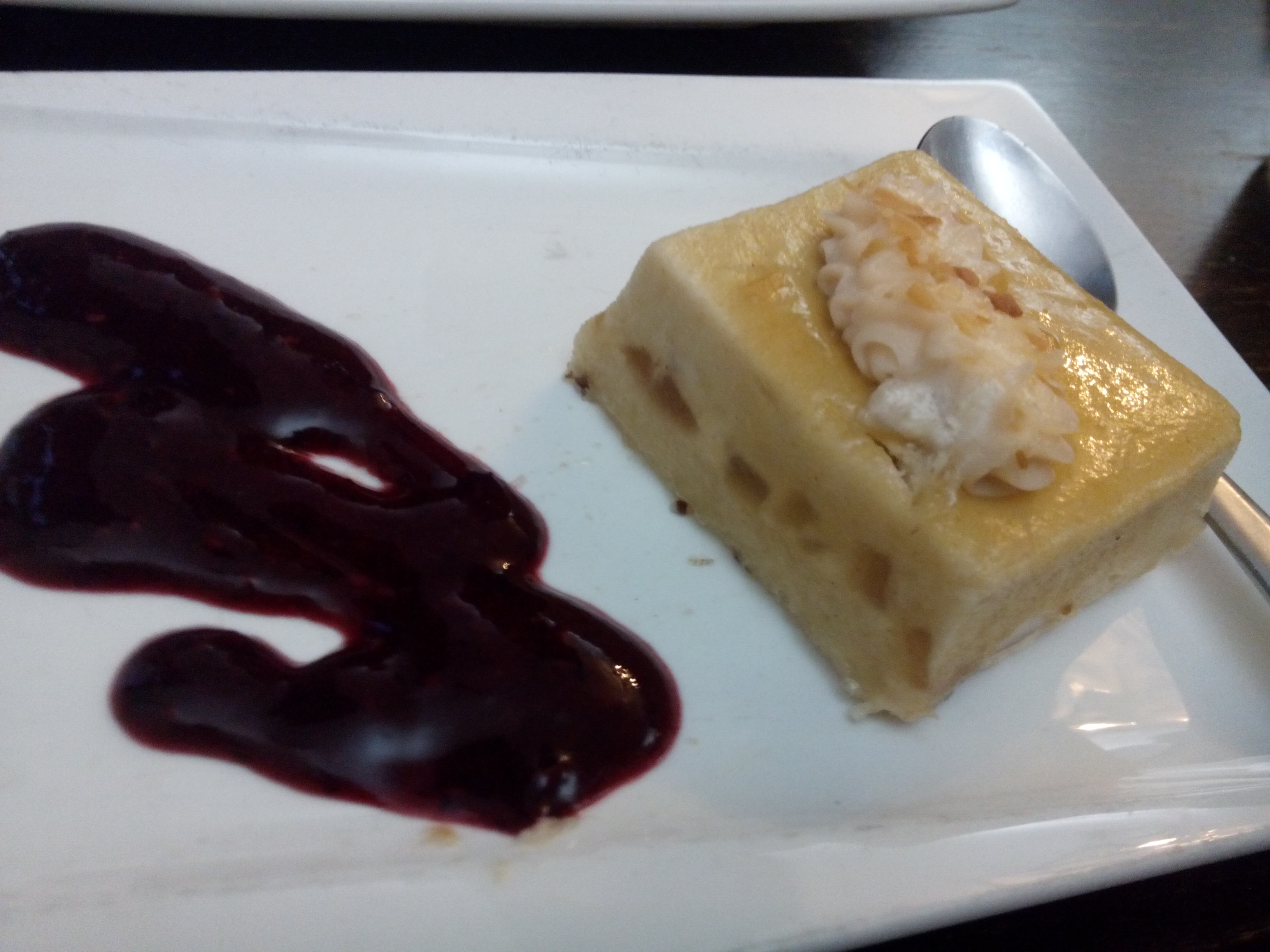 A yellow square cake next to a blob of fruity sauce