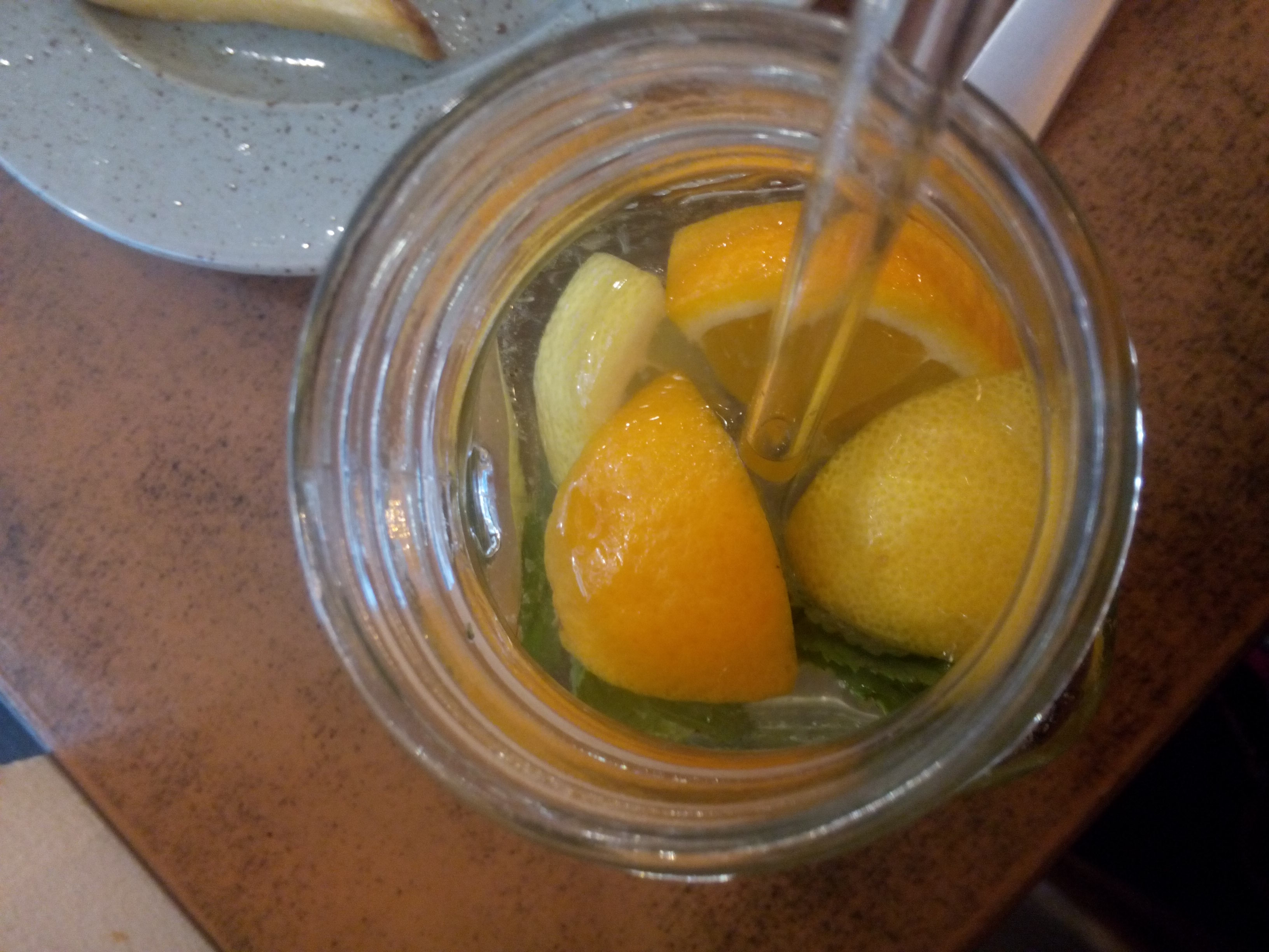 From above, a glass with a glass straw, and pieces of orange and lemon floating