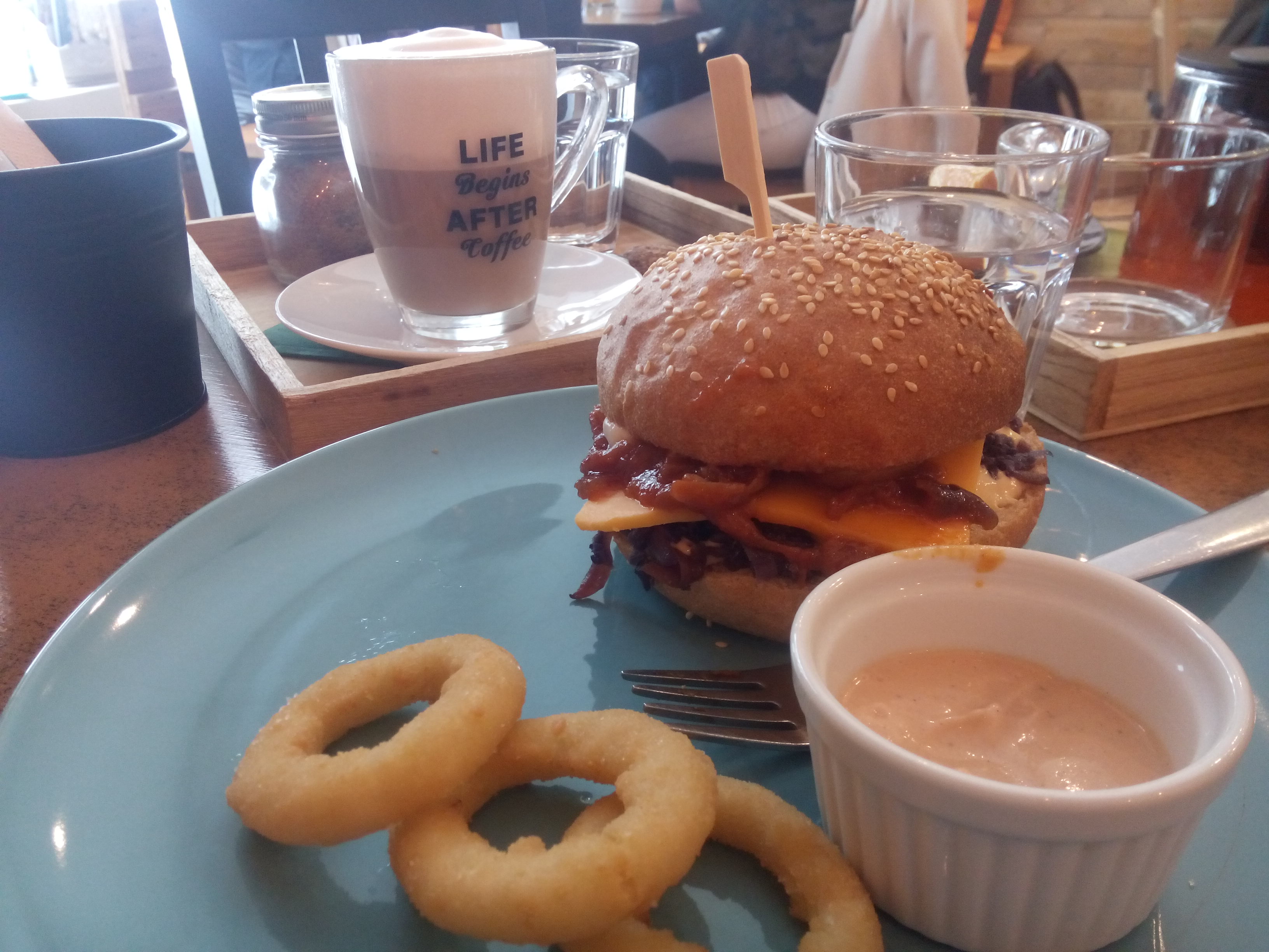 A blue plate with onion rings, a full looking burger, in front of a foamy latte