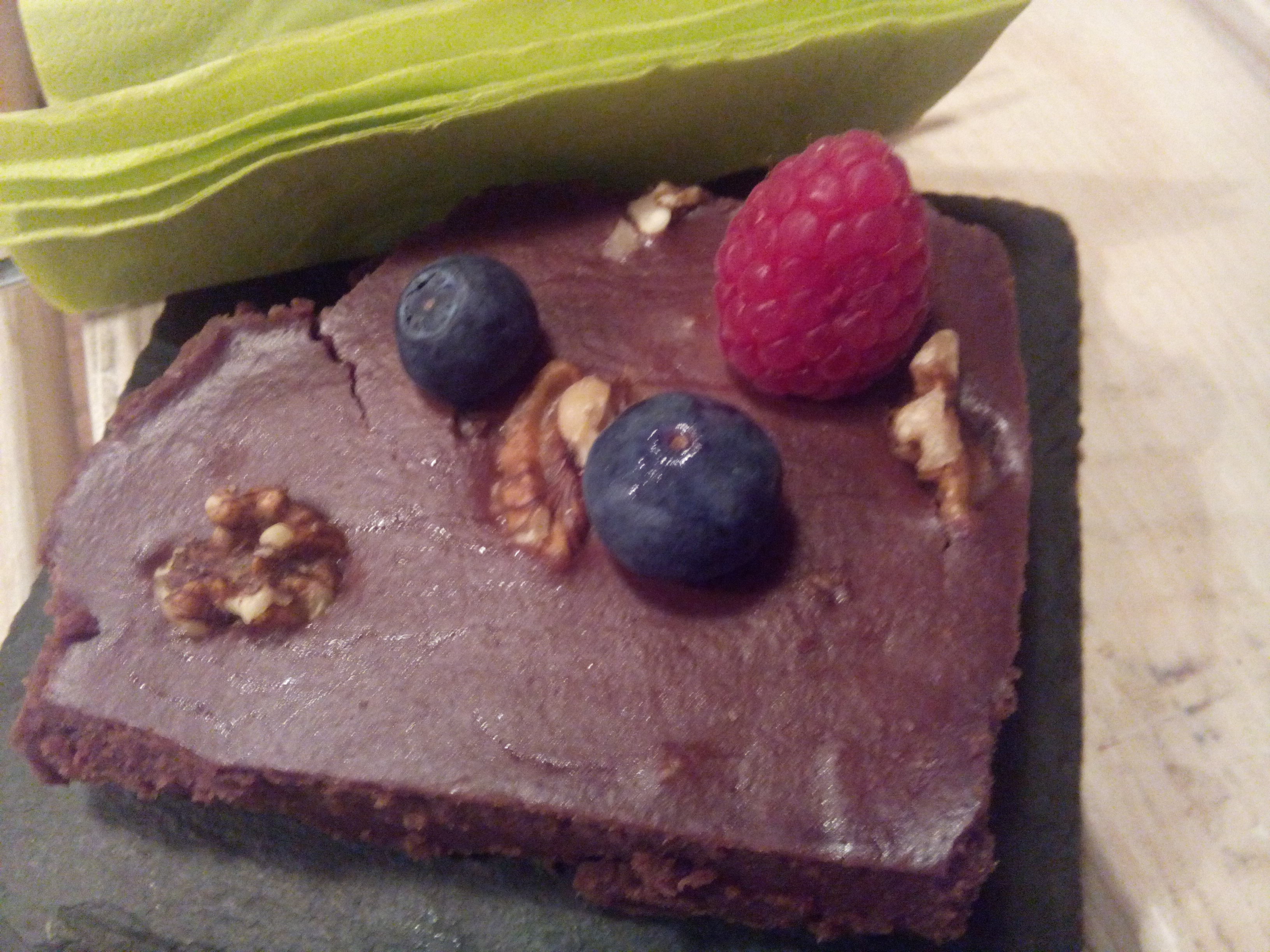 A chocolate cake with nuts, blueberries and a raspberry on top