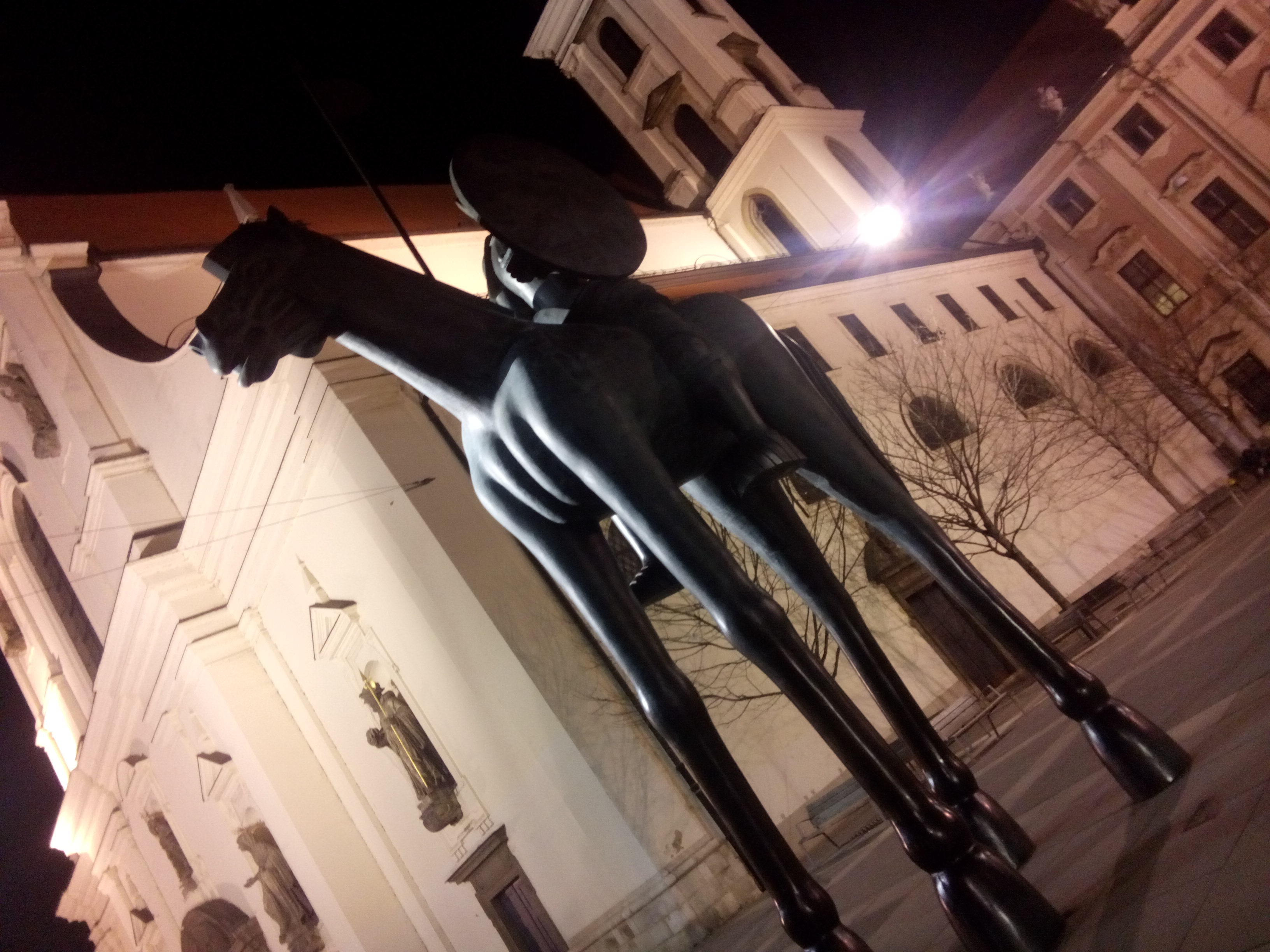 A statue of a black horse with extra long legs, in front of a white church