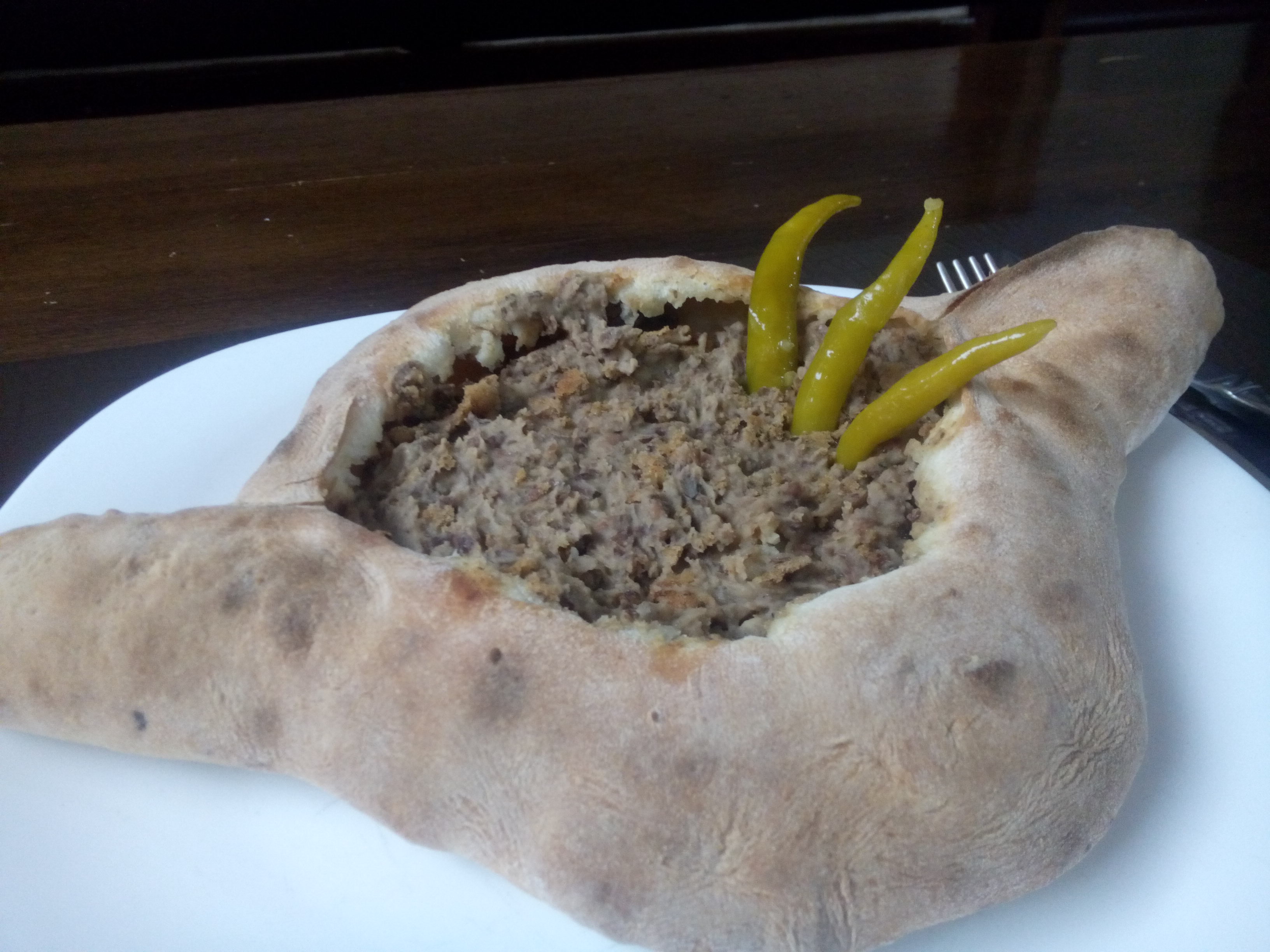 A plate with a giant hunk of bread carved out and filled with bean mush, with three pickled chillis sticking vertically out