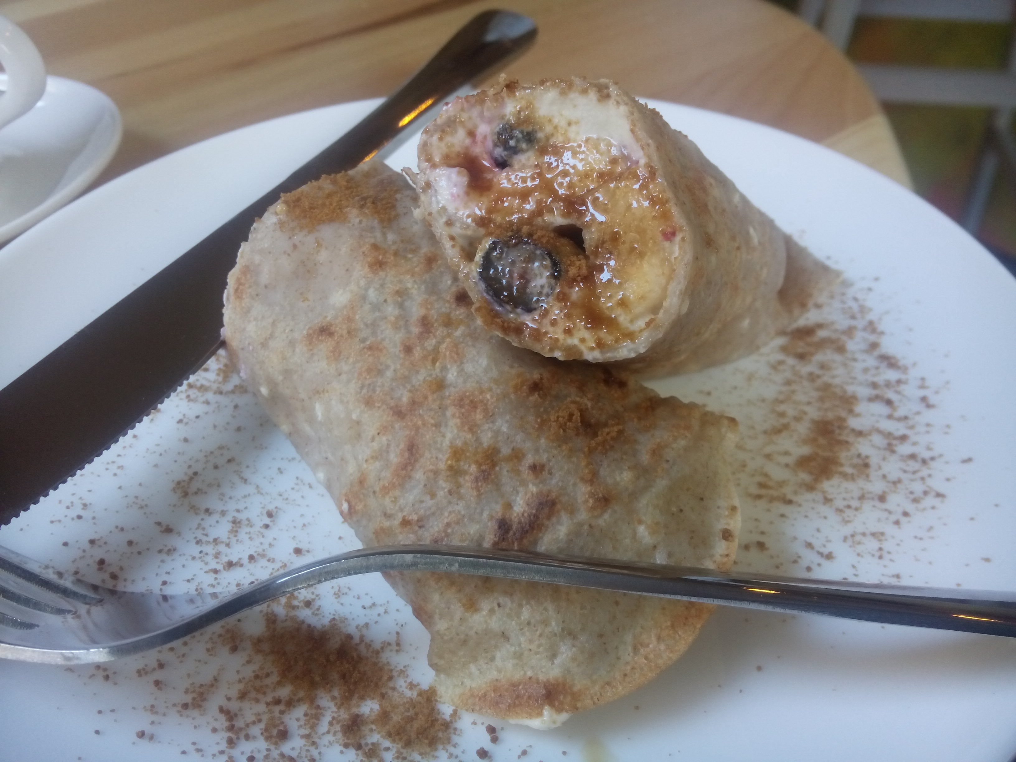 Two small pancake rolls on a white plate with scattered cinnamon and berries peaking out