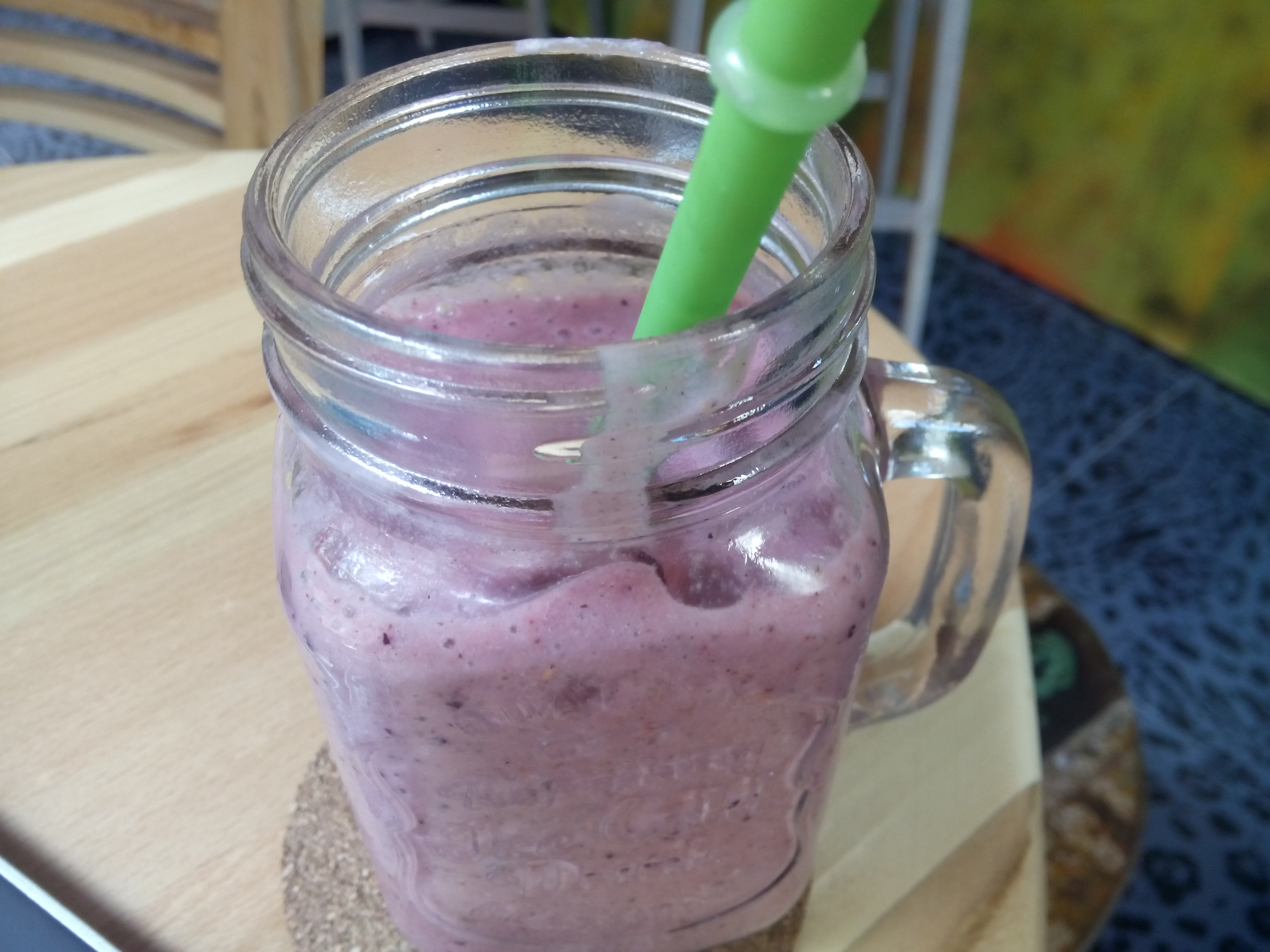 A glass jar cup with pink smoothie and a straw