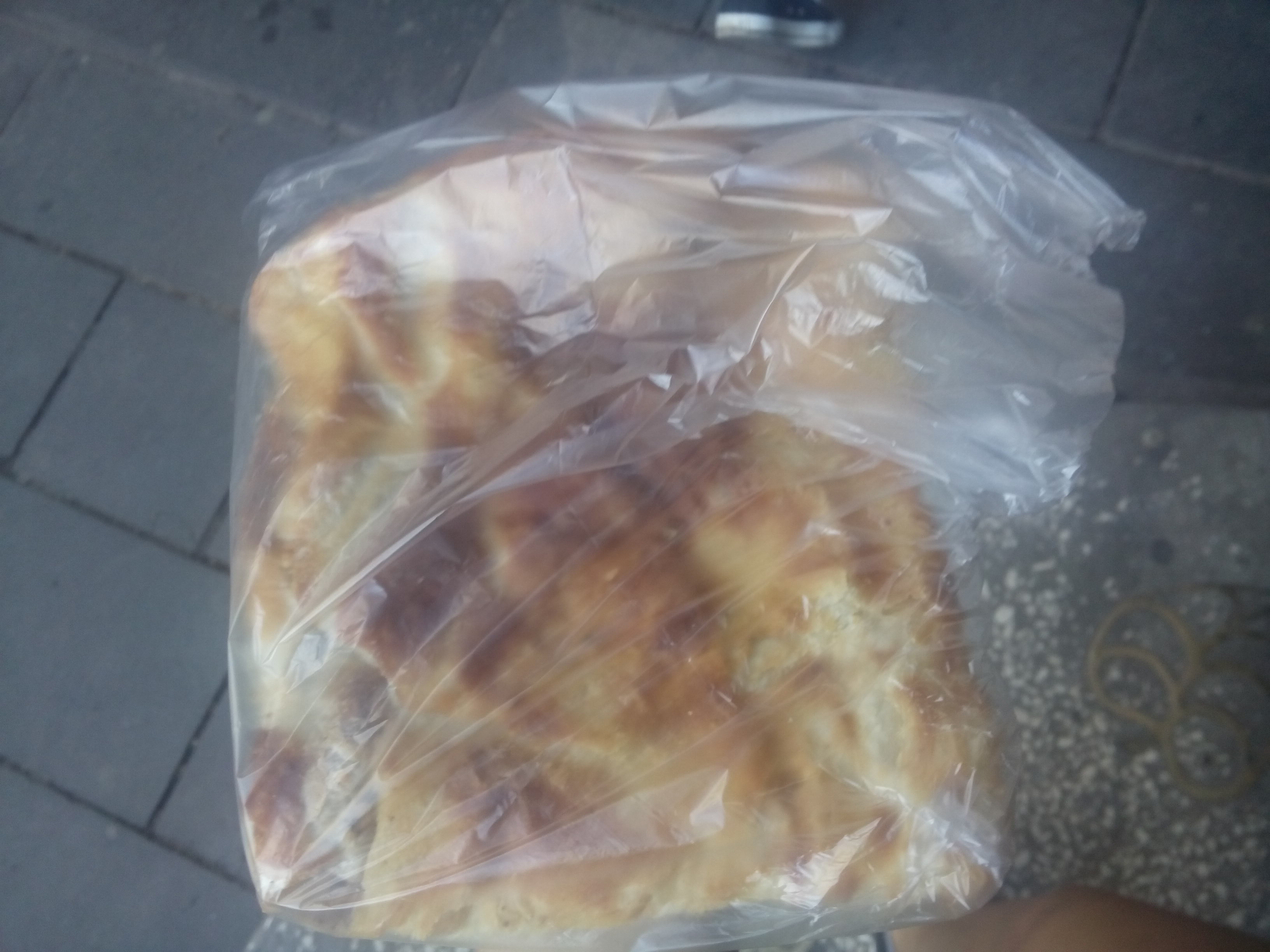 A plastic bag with a pastry in seen from above held over a pavement