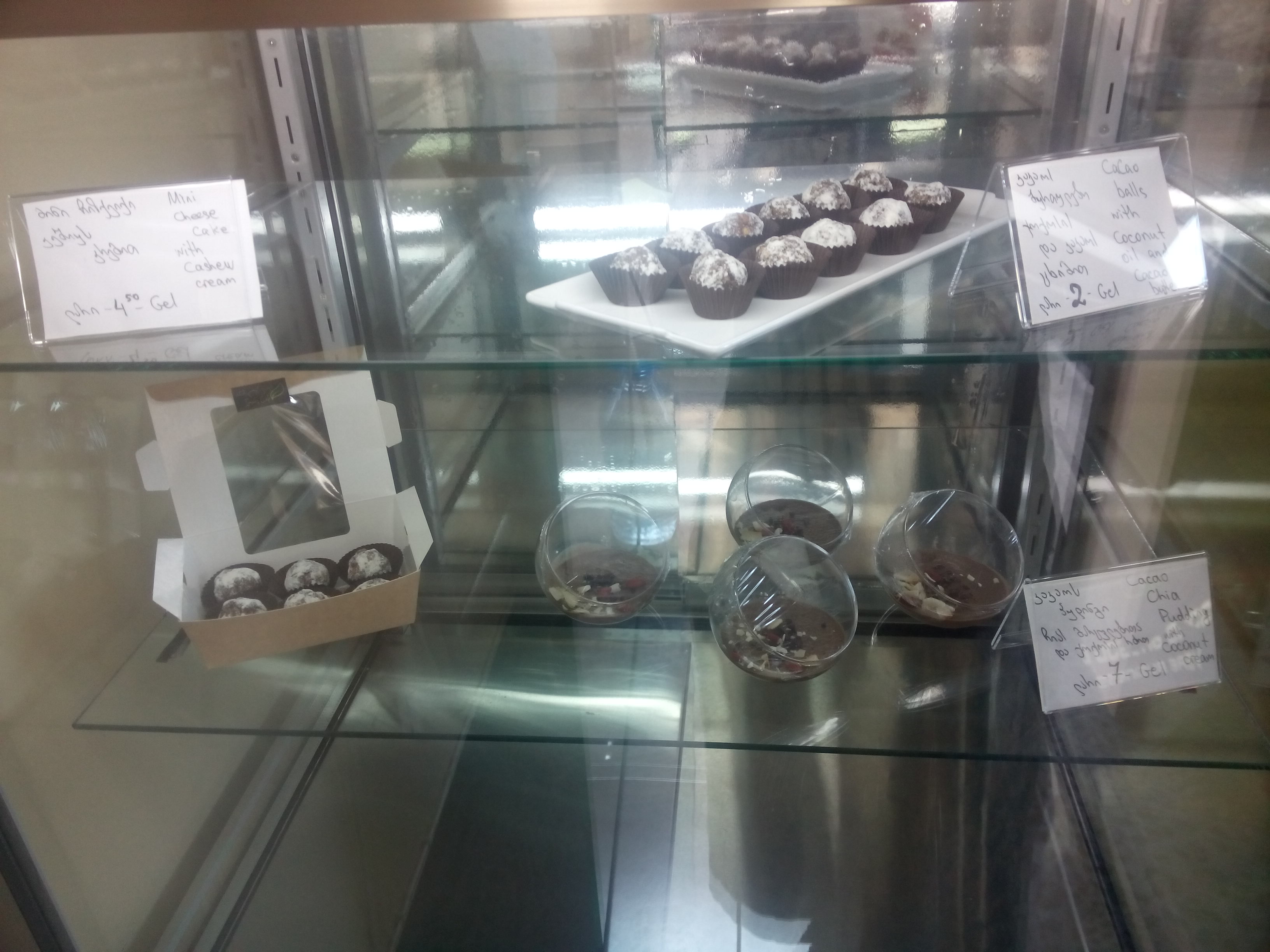 A glass cabinet with lots of light reflections, inside of which are a selection of small cakes