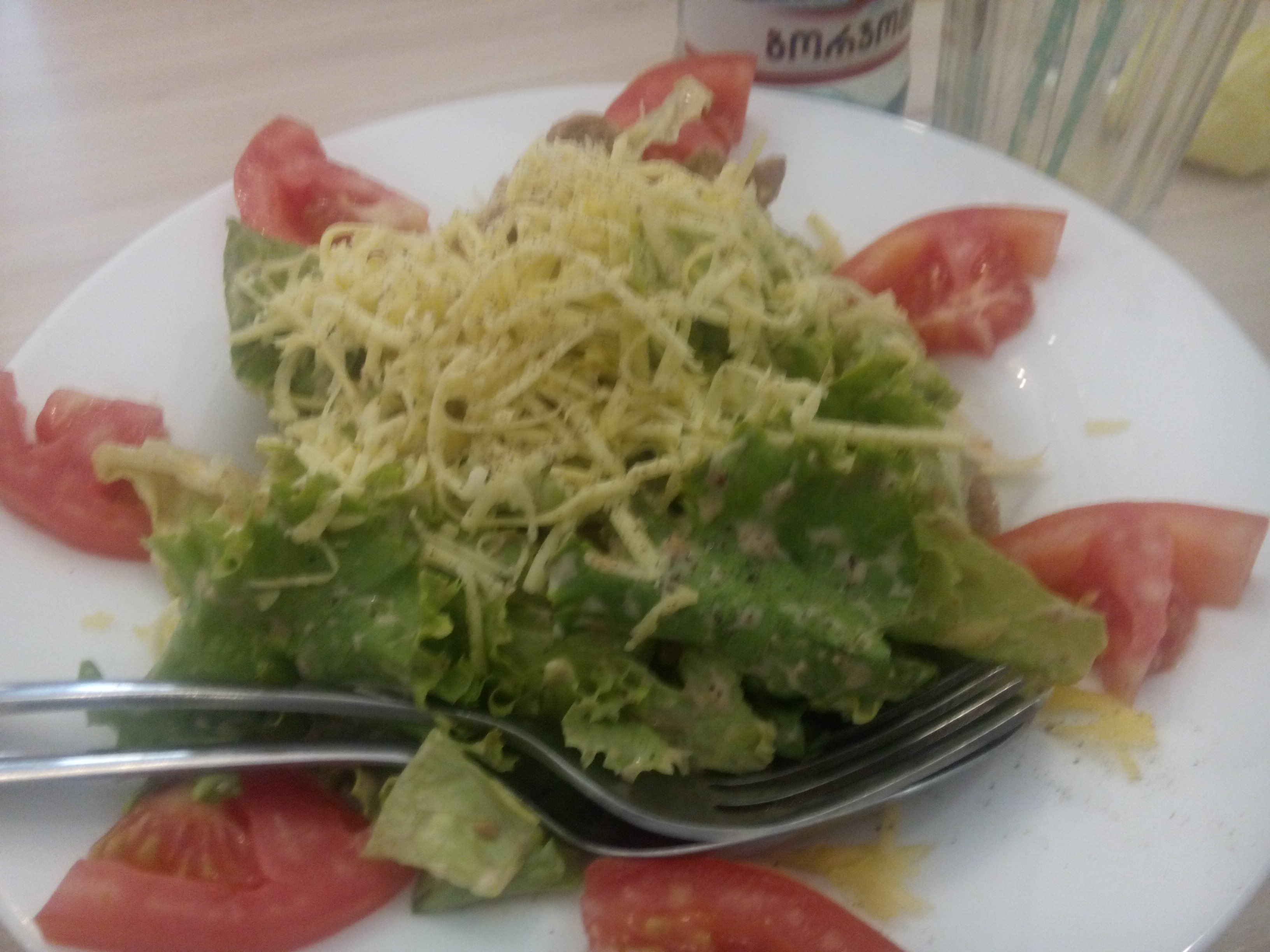 A plate of lettuce with tomato slices fanning out, and not-cheese grated on top