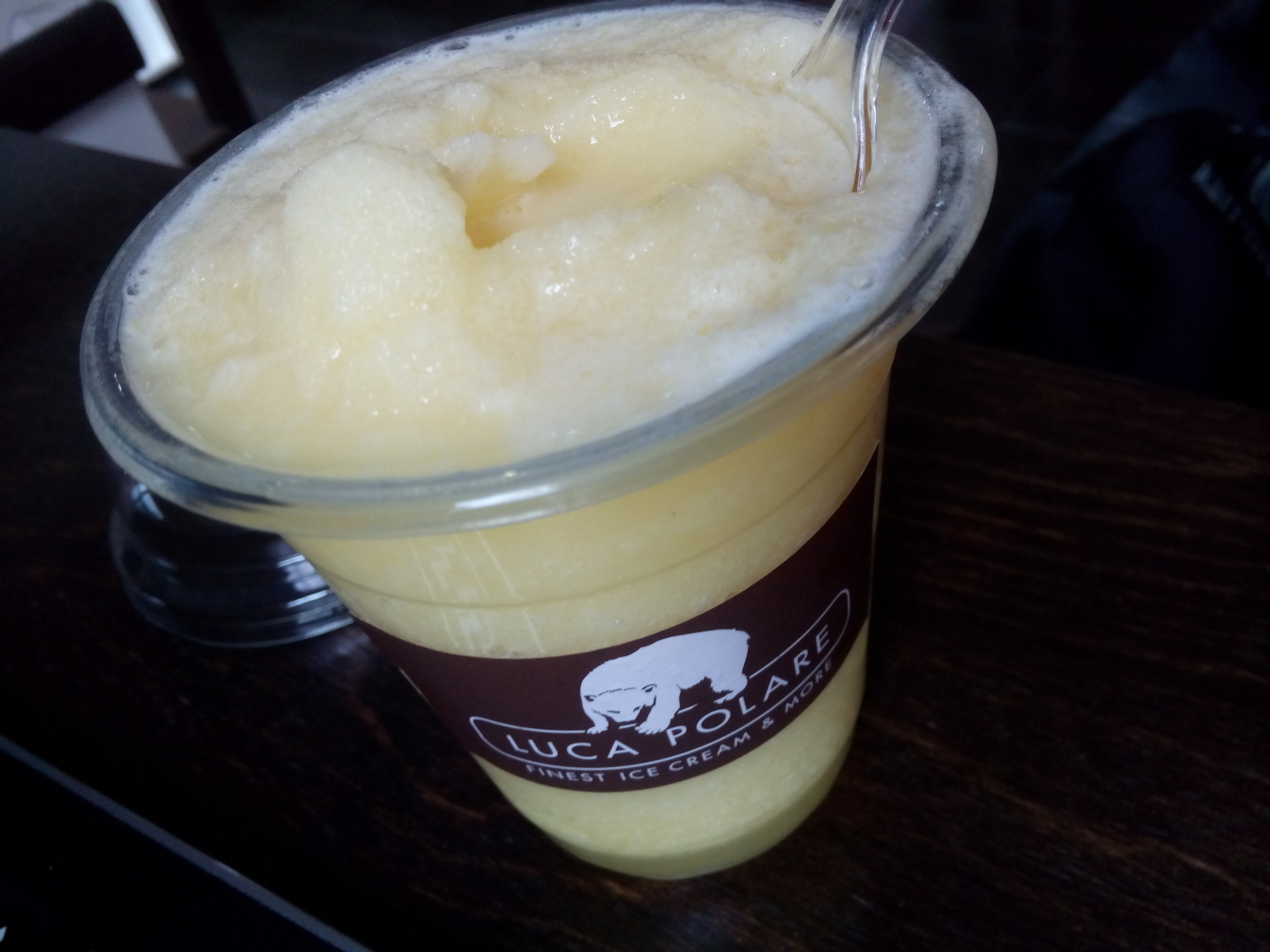 A plastic cup with a brown Luca Polare label, containing yellow slush