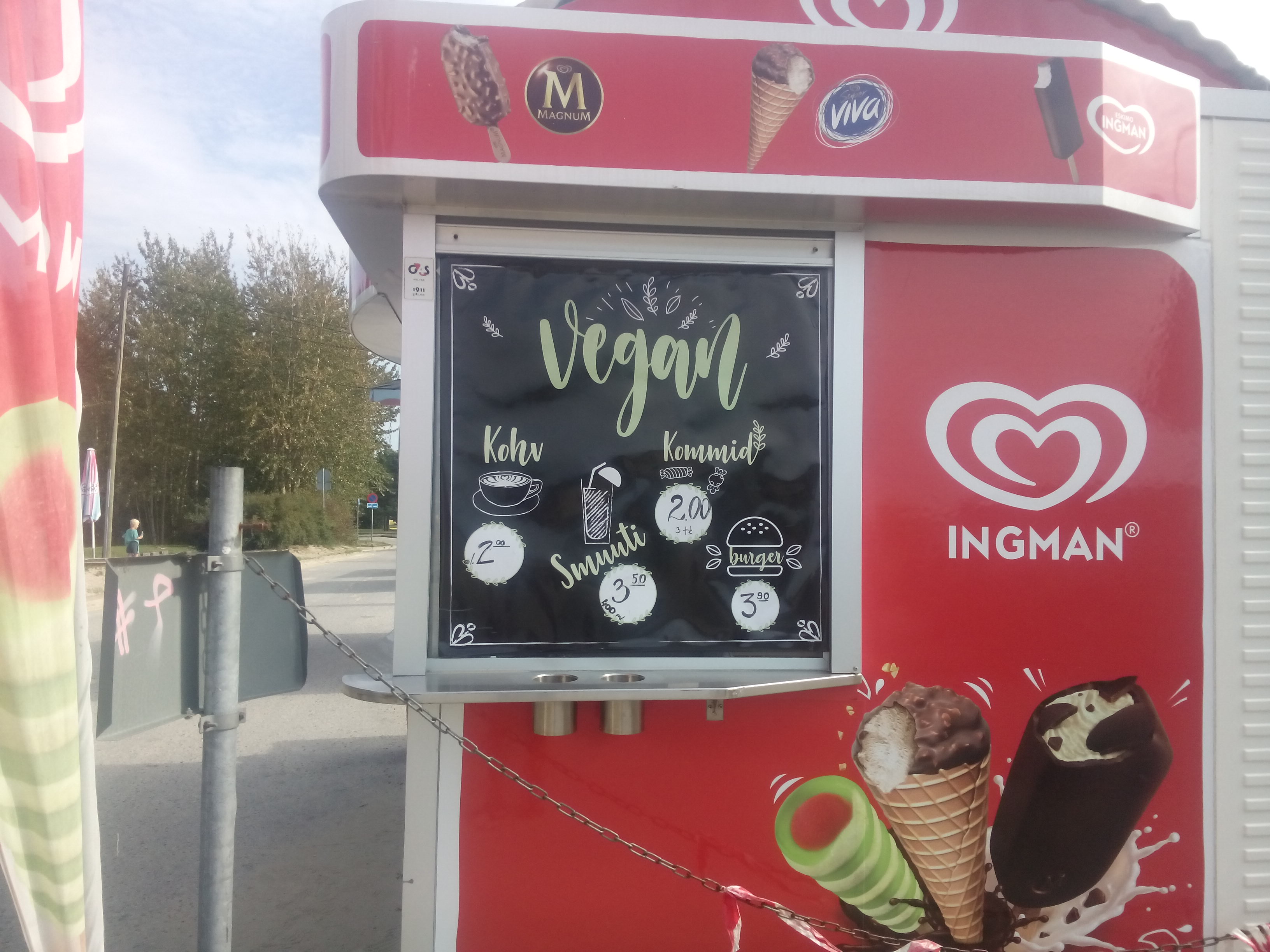 A side view of a food kiosk with the red and white Wall's logo, pictures of ice creams, and a separate vegan menu