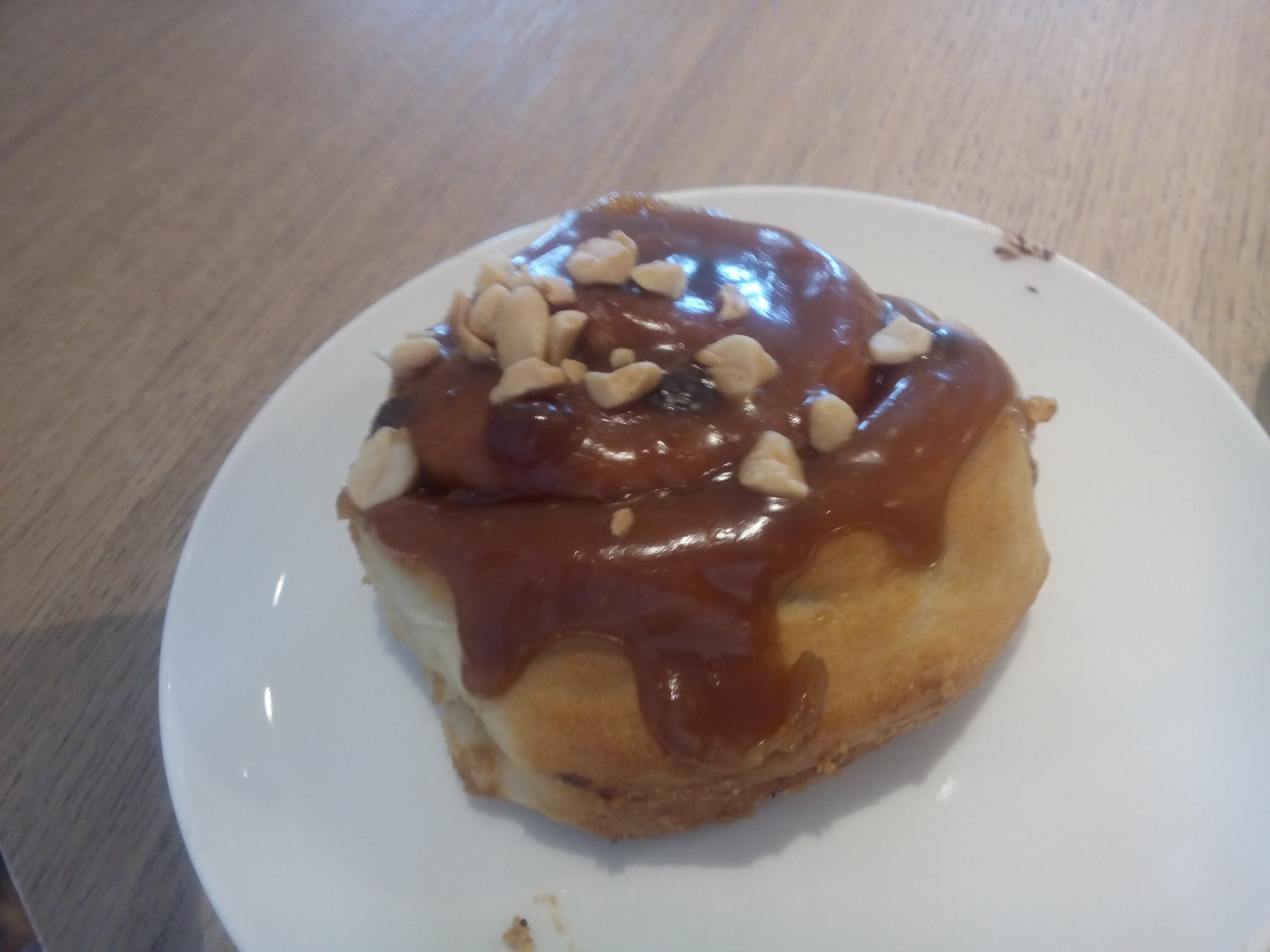 A white plate with a round fat sticky caramely bun with nuts on