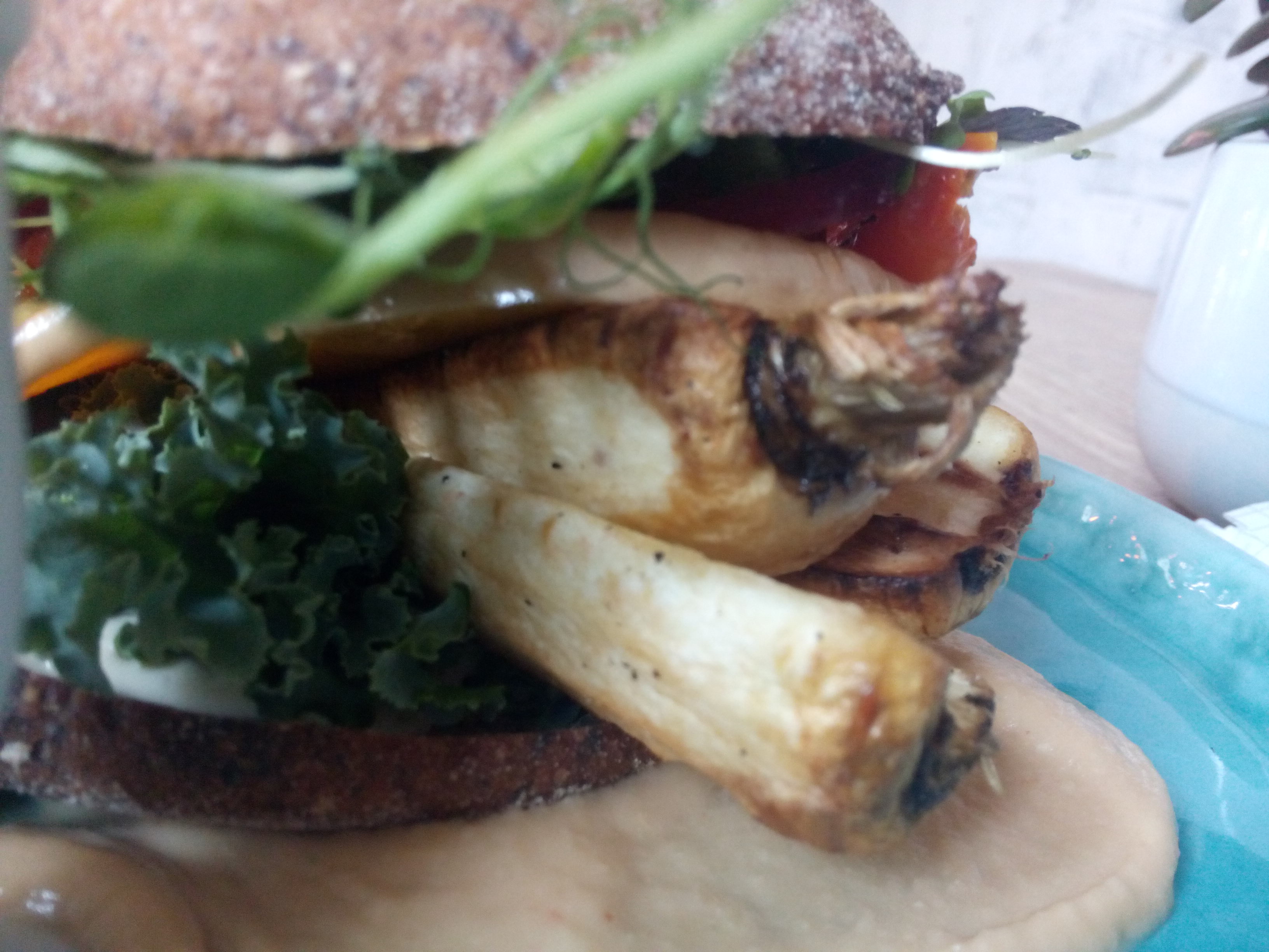 Close up of root vegetable burger, with parsnips and kale poking out from the bread