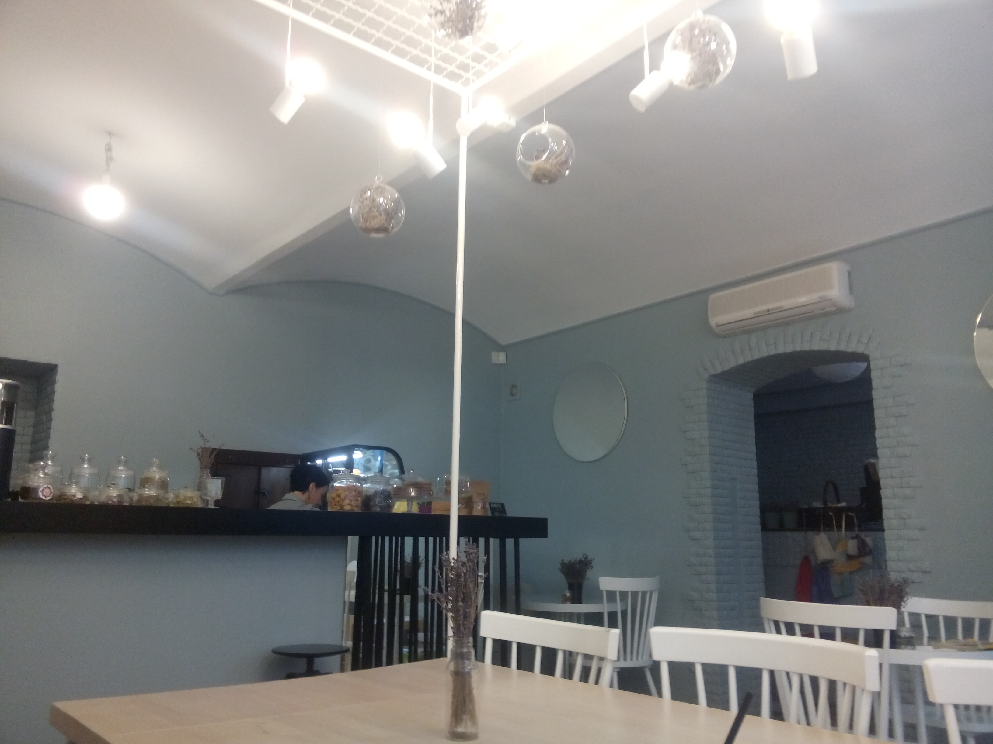 Inside a cafe painted blue with wooden tables, white seats and a counter with jars on