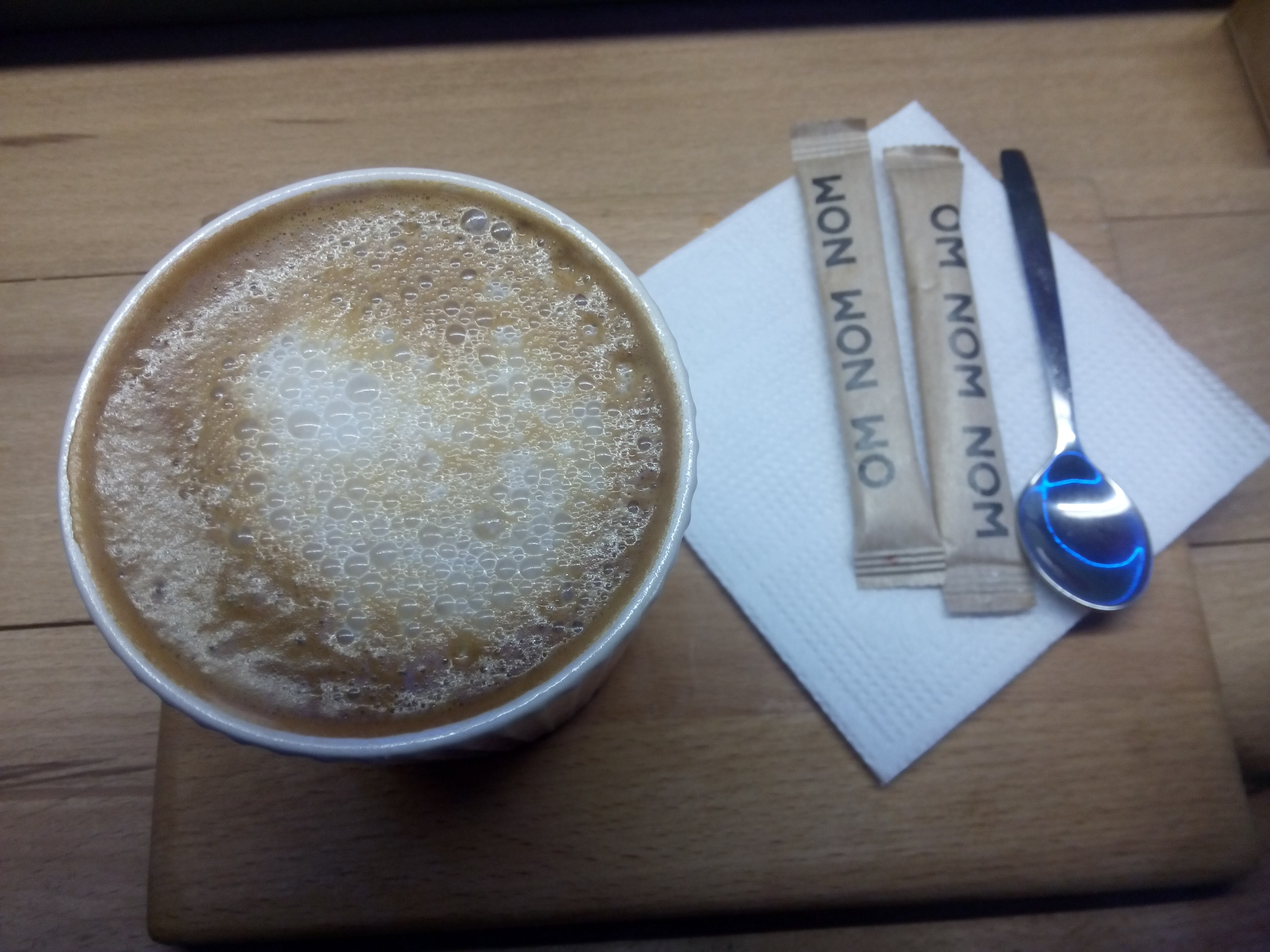 Top view of a foamy coffee drink, next to a napkin and sugar packets