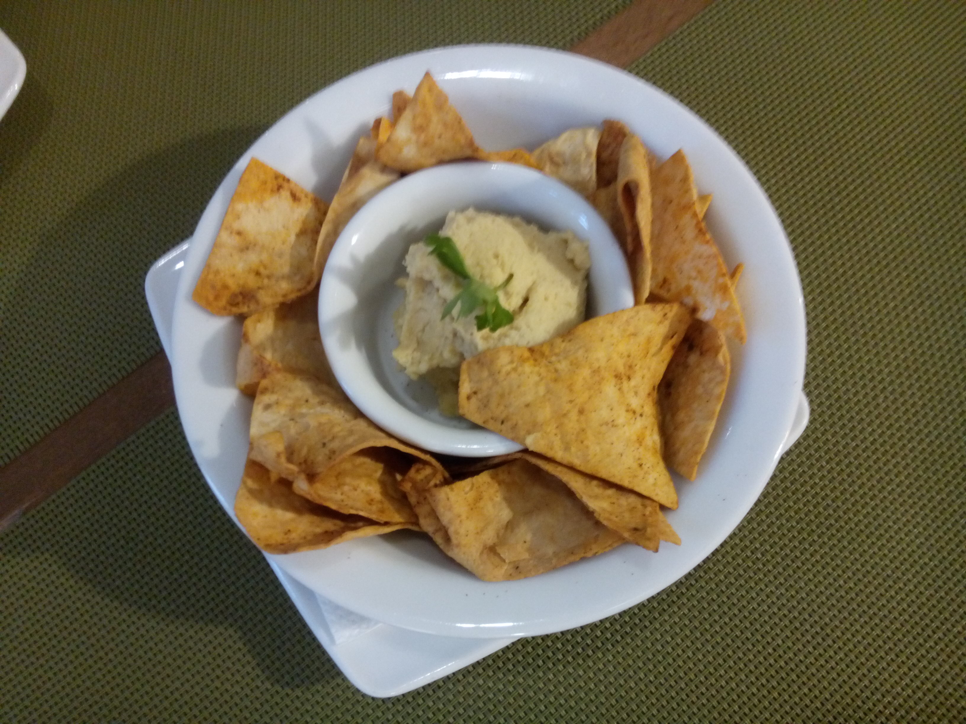 From above, a round dish with corn chips around the edge and a small ball of hummus in the middle