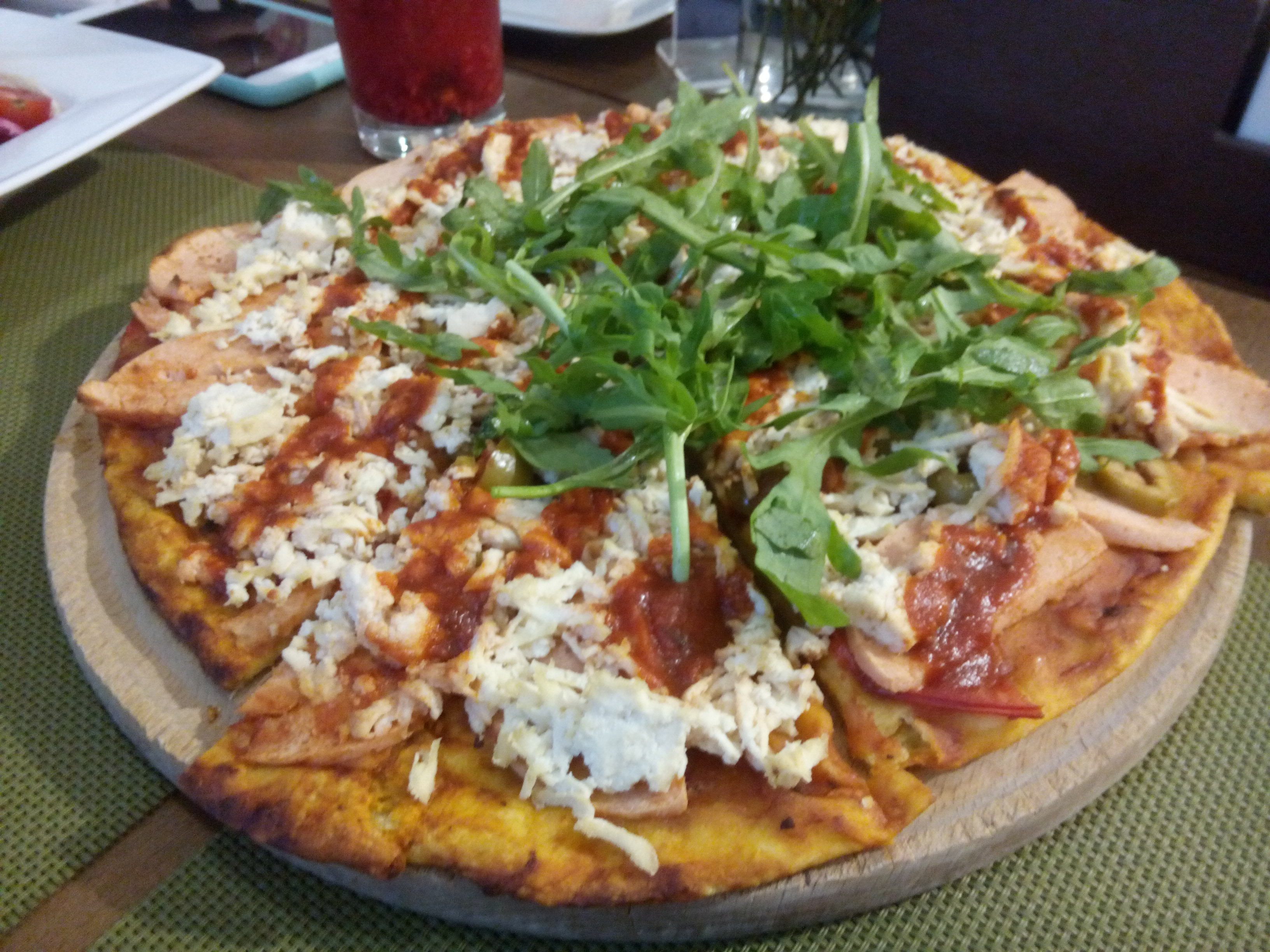A large pizza with seitan, tomato, vegan cheese, scattered greens