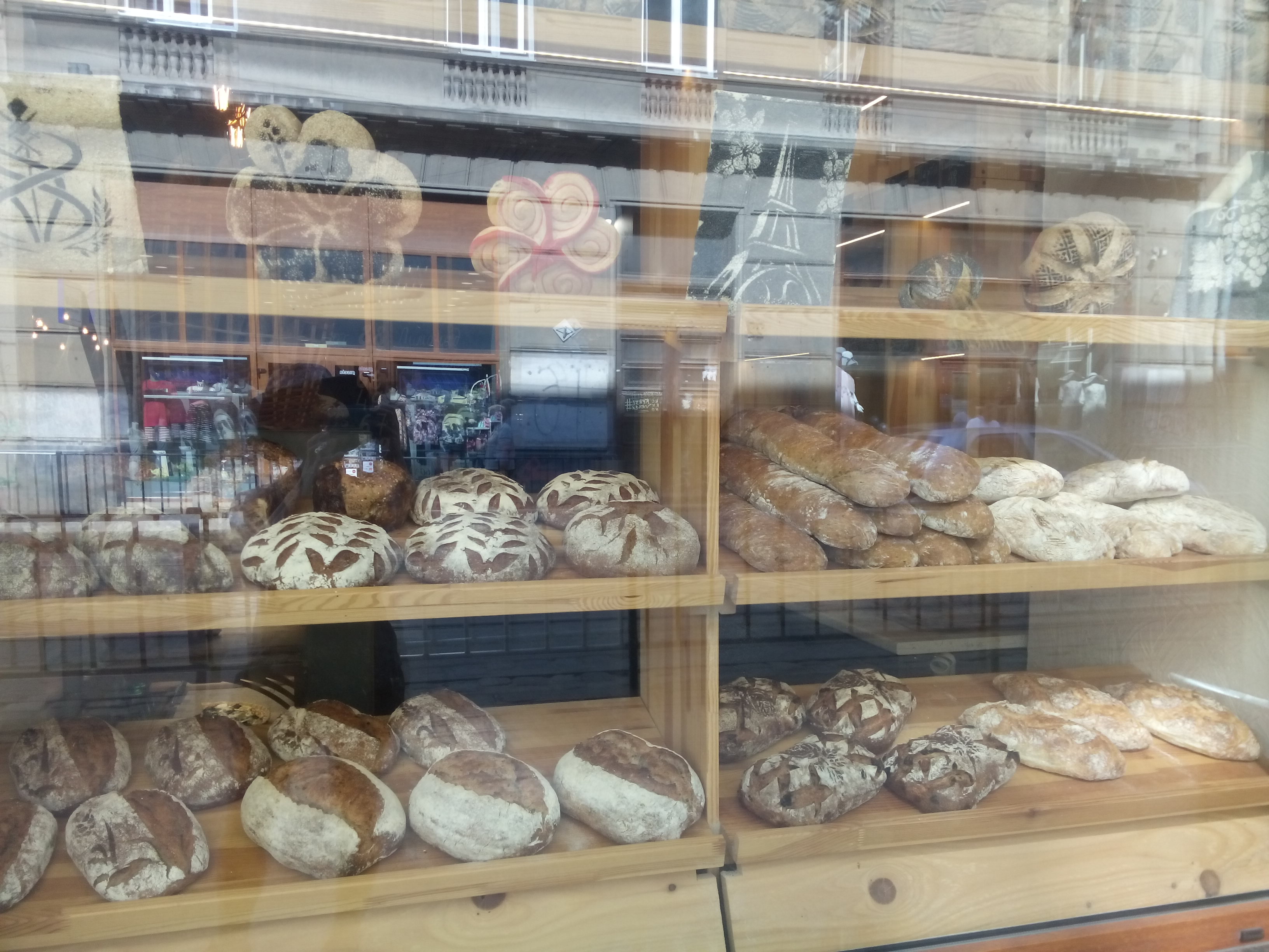 A reflecty glass window with wooden shelves of fresh bread