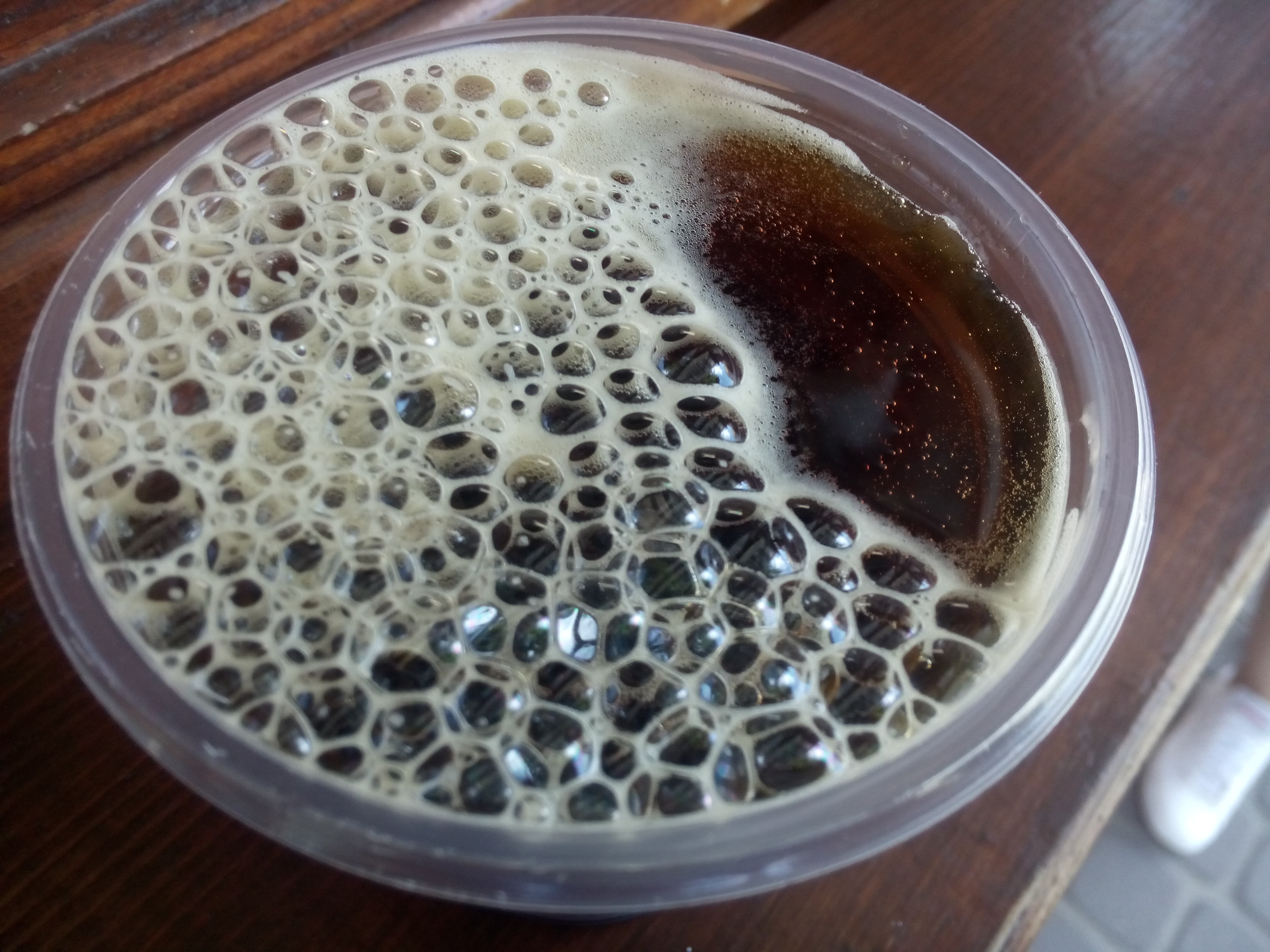 A plastic cup with brown bubbly foamy liquid