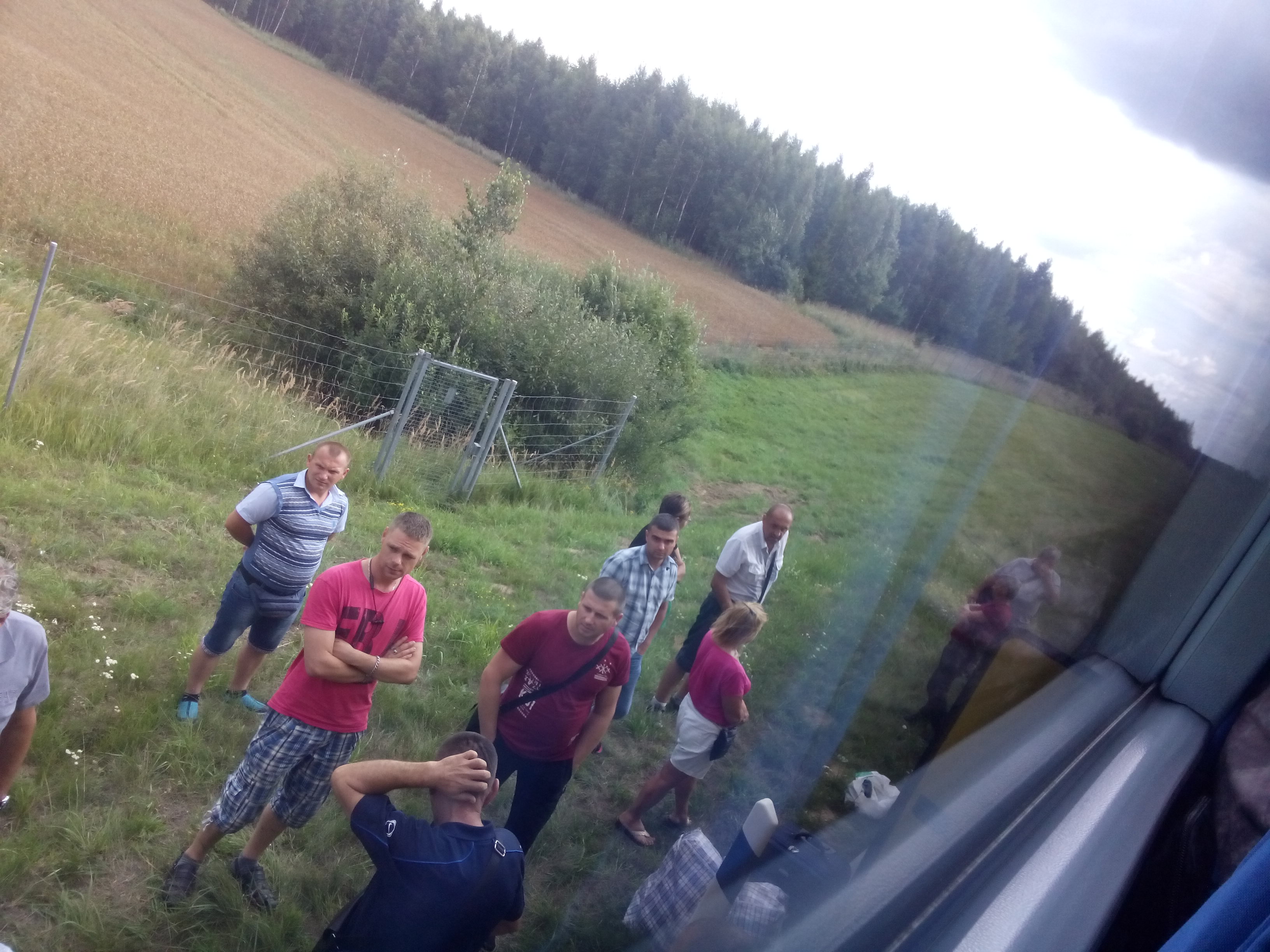 A view from inside a bus of people standing on a grassy verge on a cloudy day