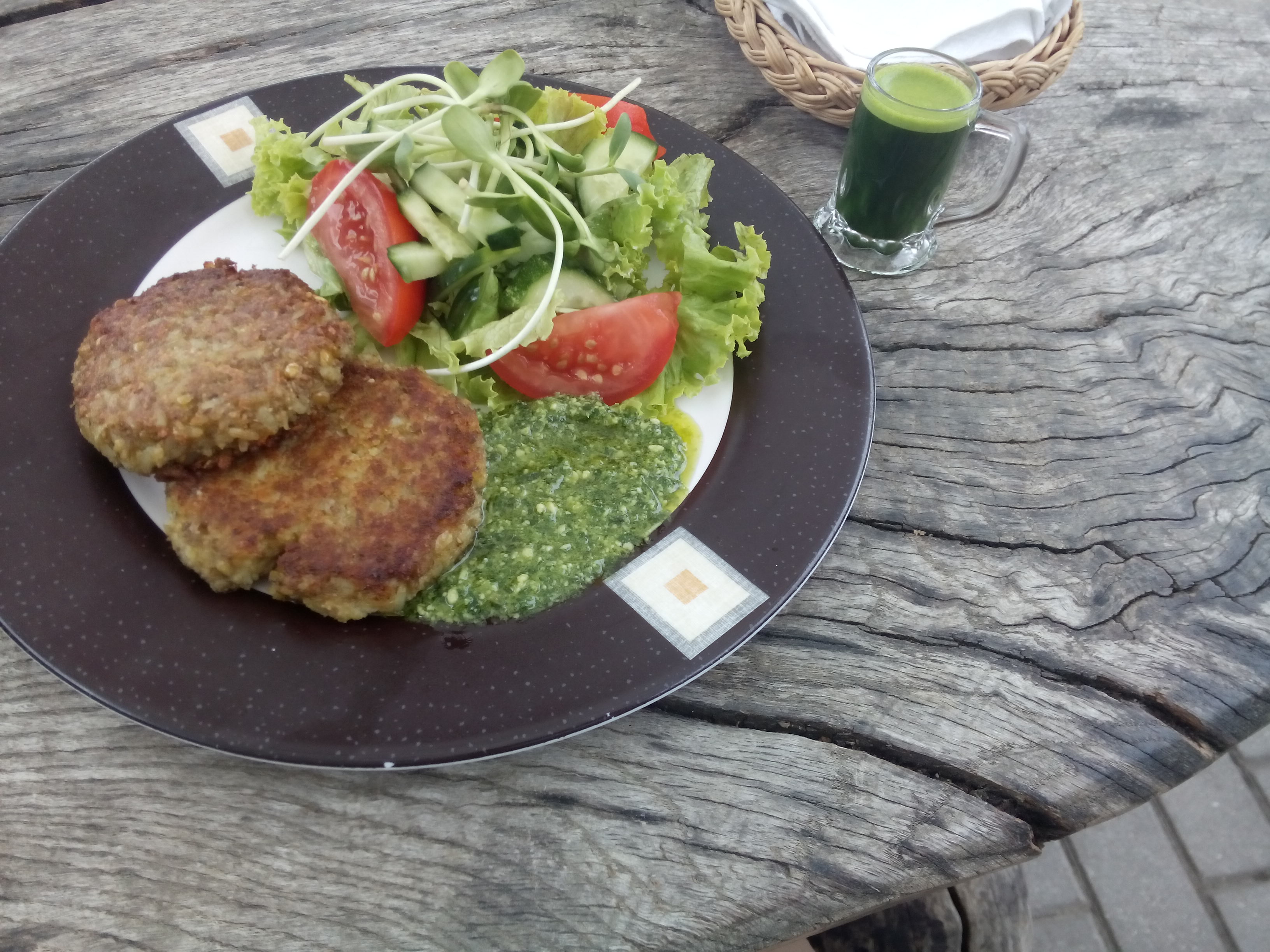 A plate on a rough wooden table holds round lentil patties and salad
