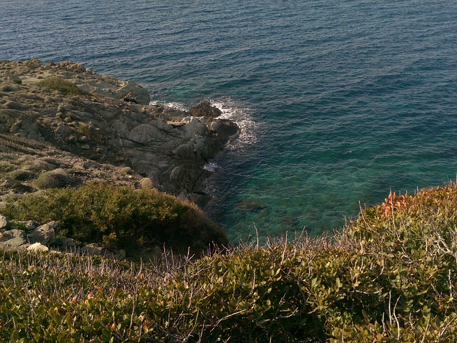 Looking down on clear green blue sea breaking on rocks