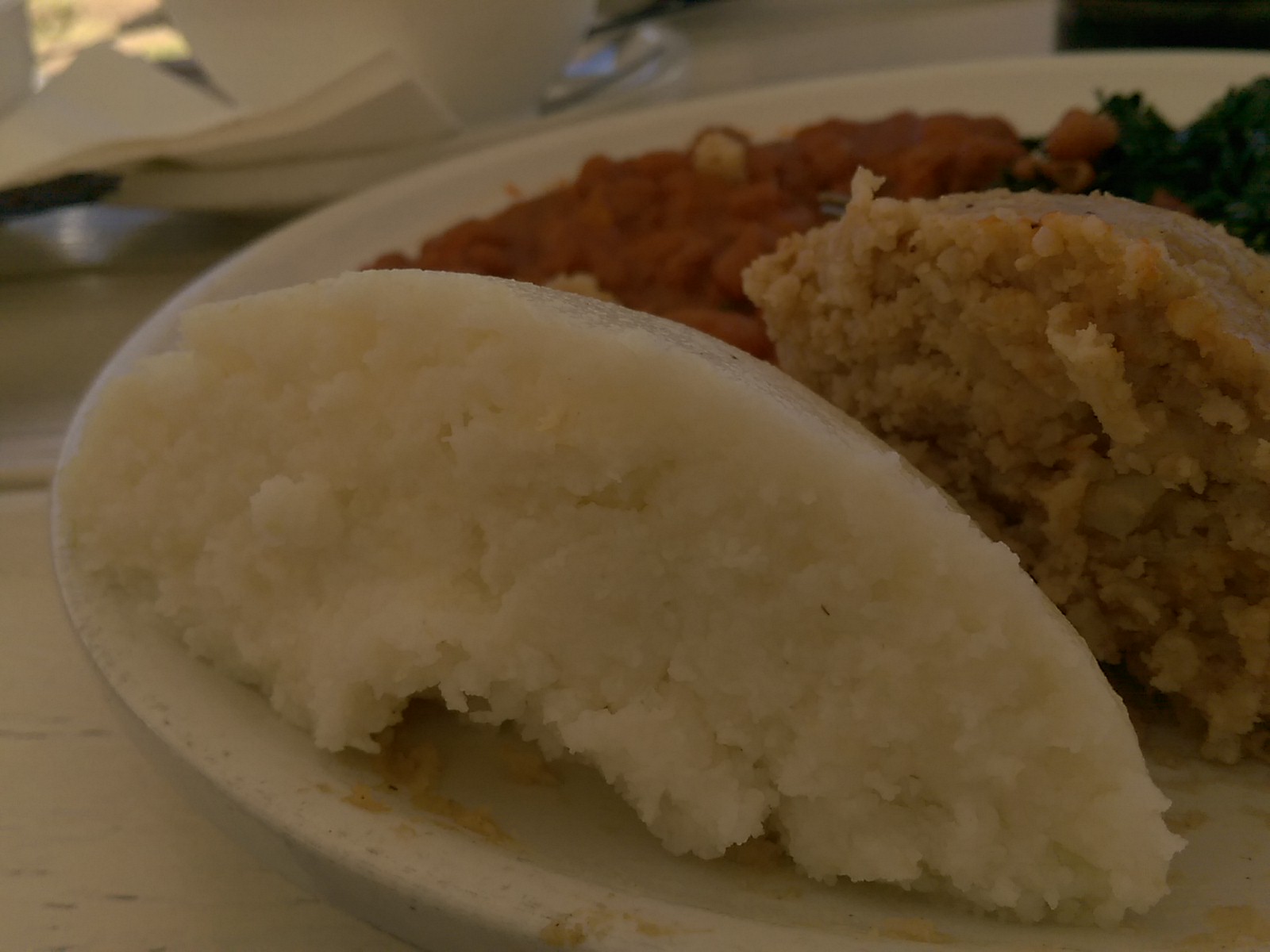 Closeup of half a ball of white sadza on a plate with peanut rice and beans