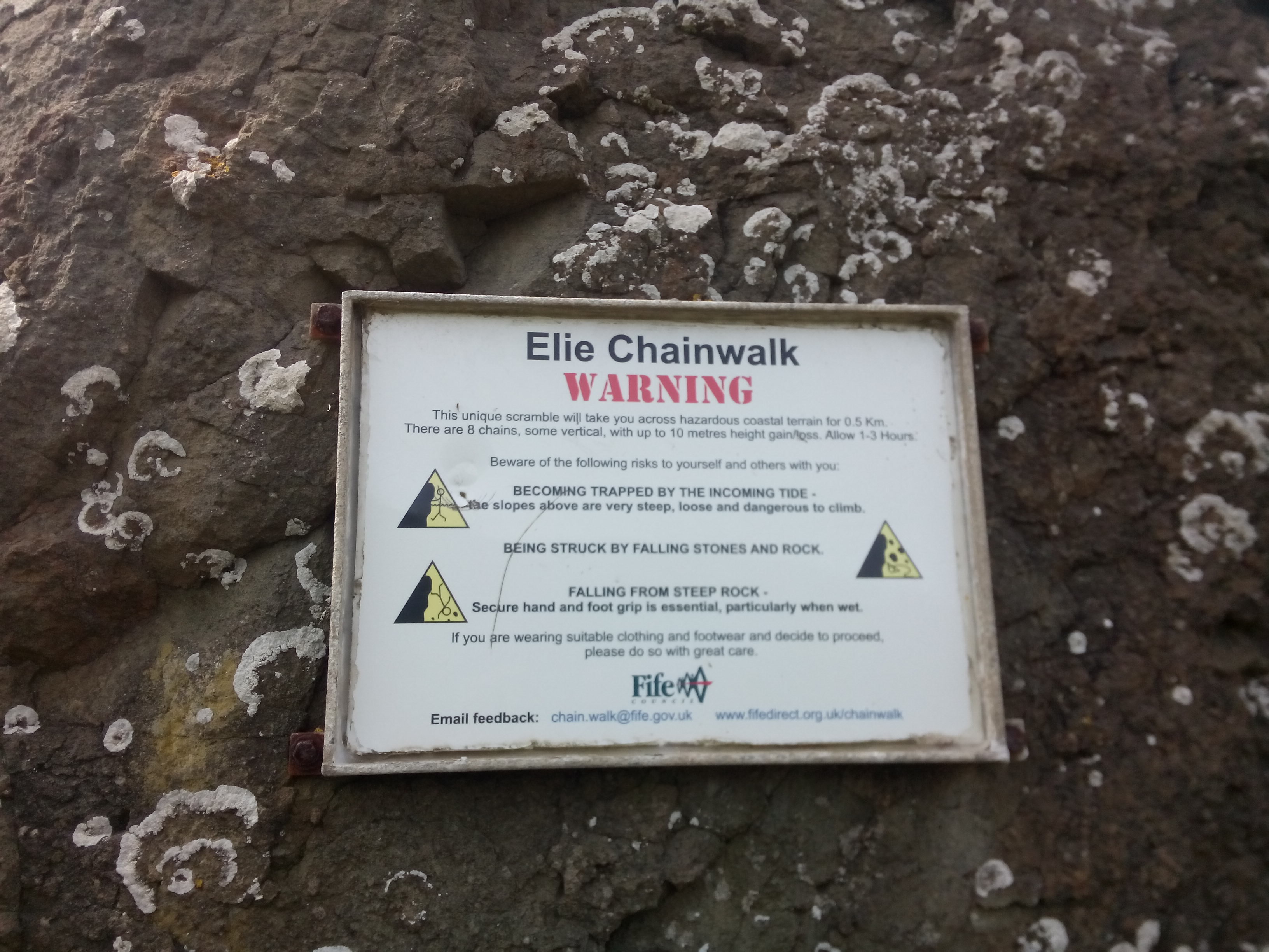 A sign on a rock WARNING about the Elie Chainwalk