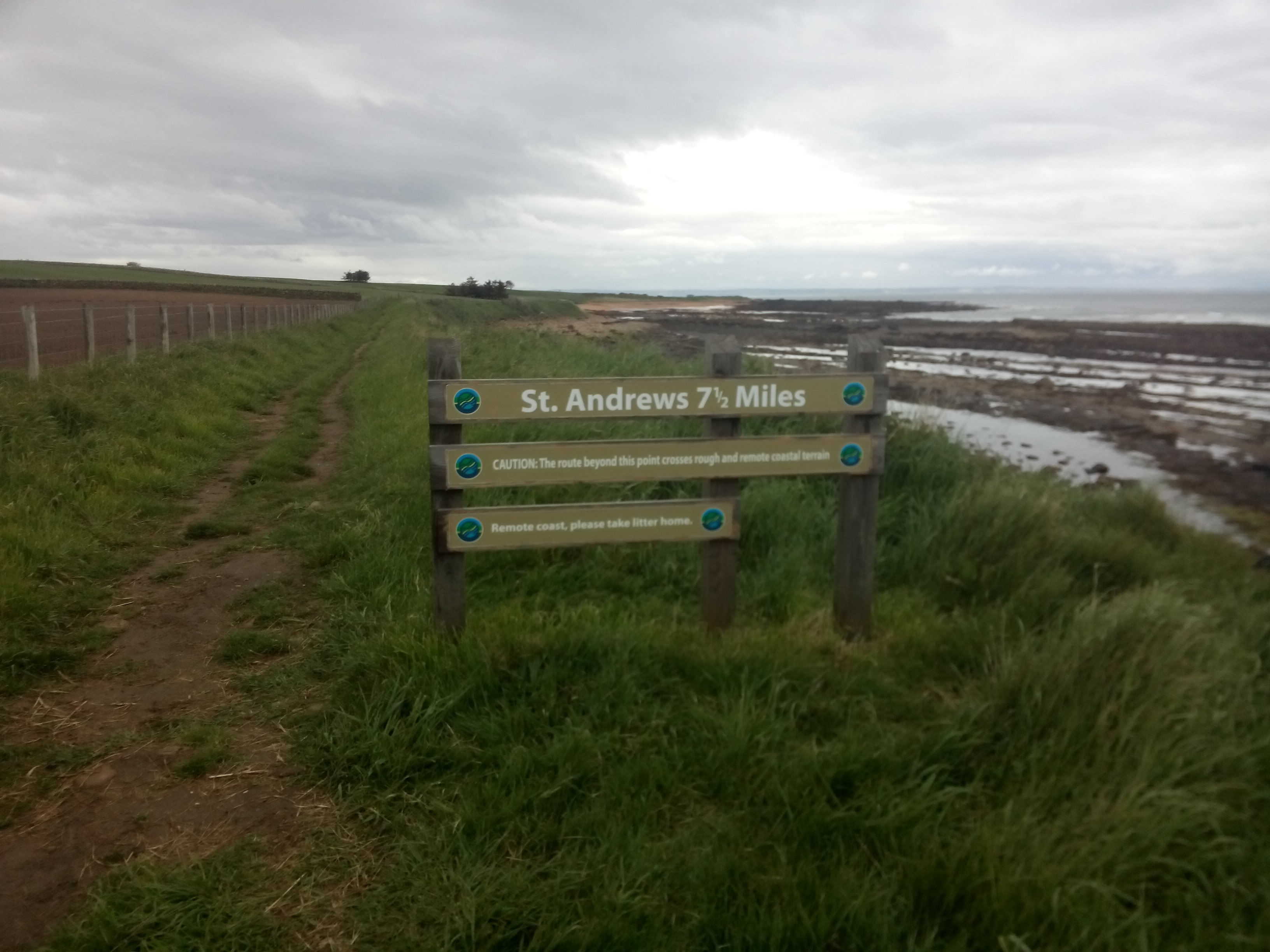A wooden sign by a beachside track reads St Andrews 7.5 miles