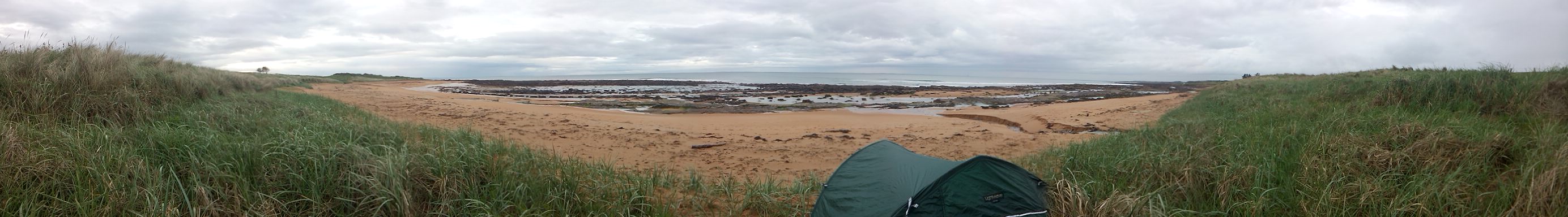 Panorama of a tent between two grassy dunes with a sandy beach and distant sea