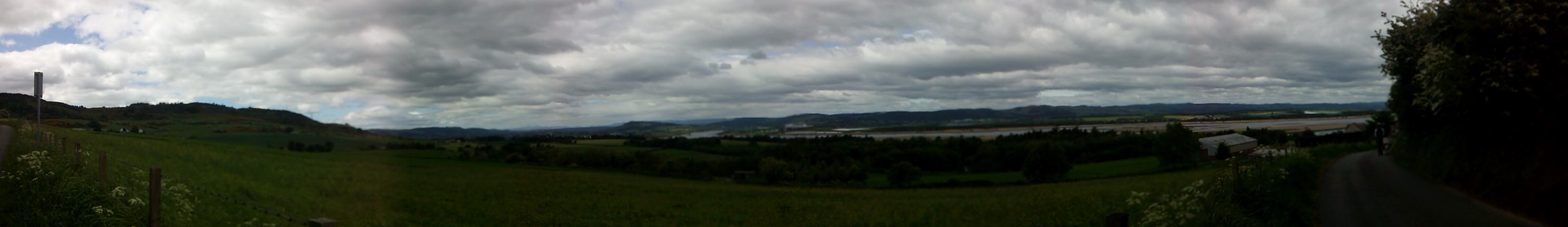 Panorama under cloudy skies, across fields, woodlands and water
