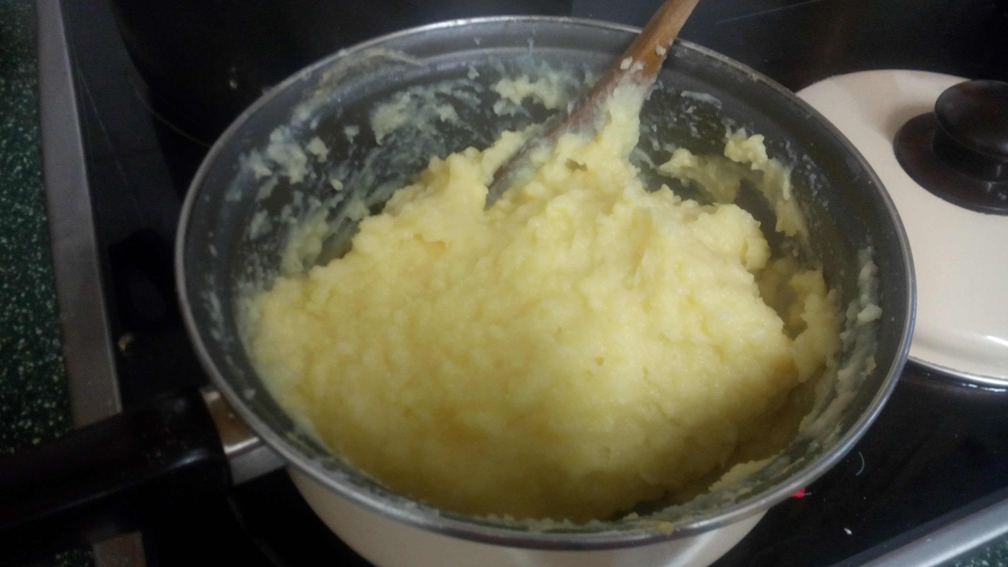 yellowish mush in a cooking pot with a spoon sticking out