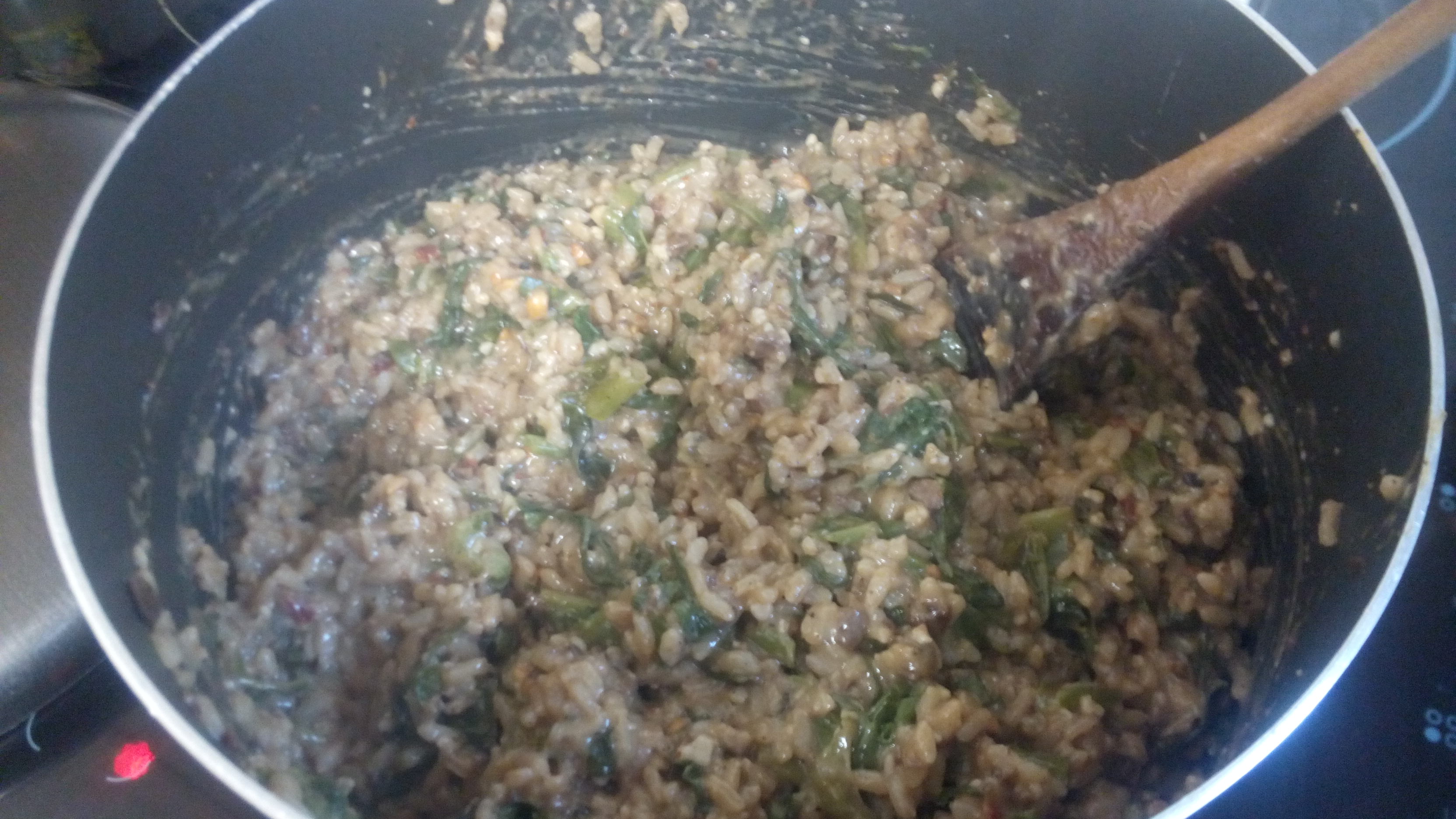 gooey rice and greens cooking in a big pot with a spoon