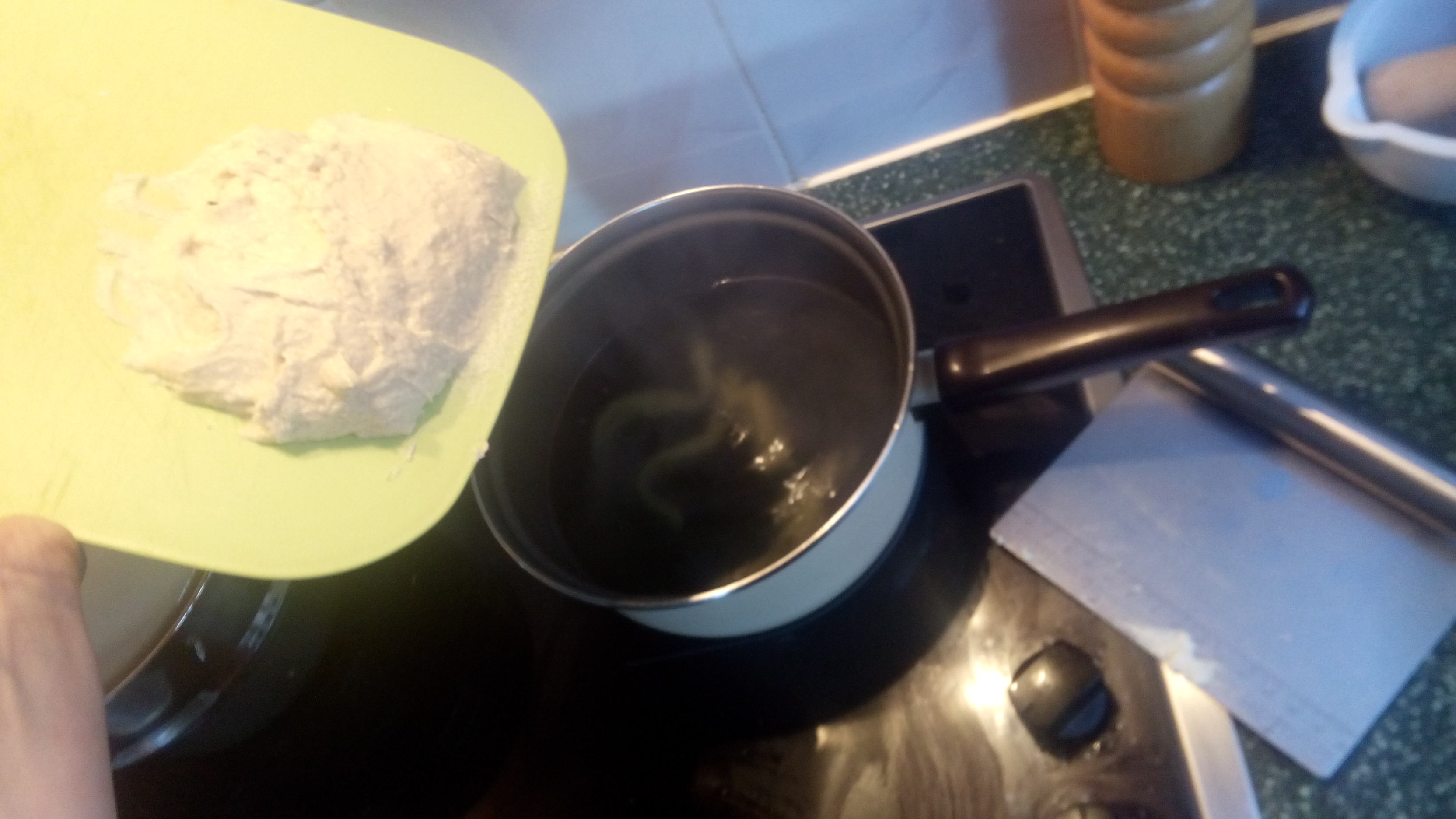 a cutting board with dough held over a pot of boiling water, beside a metal bench scraper
