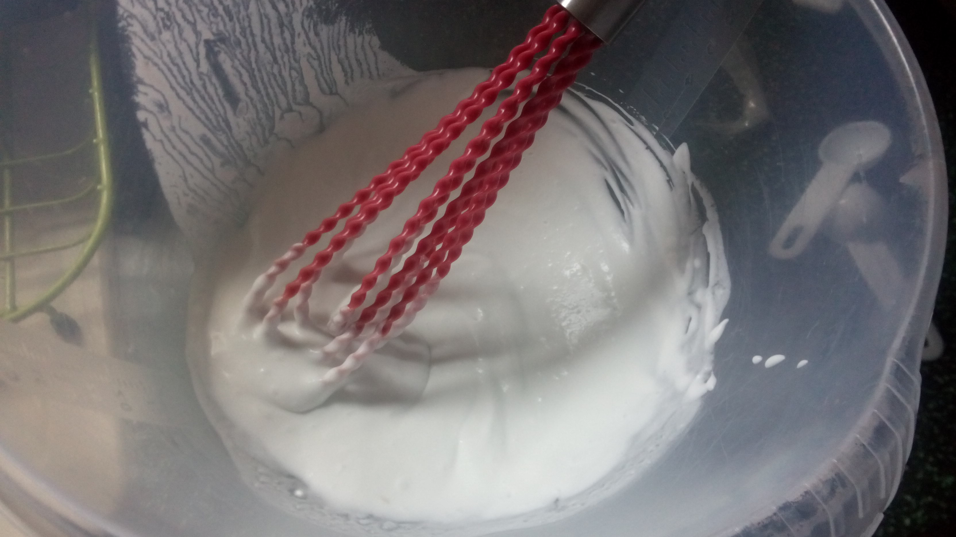a red whisk in a plastic bowl in white creamy mix