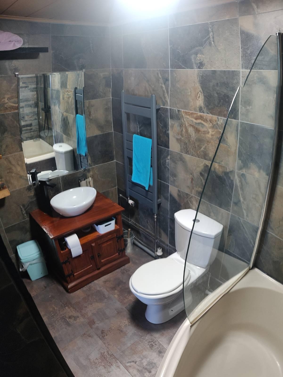 After: Bathroom with stone effect grey and brown tiles, modern white sink and toilet, mahogany colour sink cabinet, grey heated towel rail
