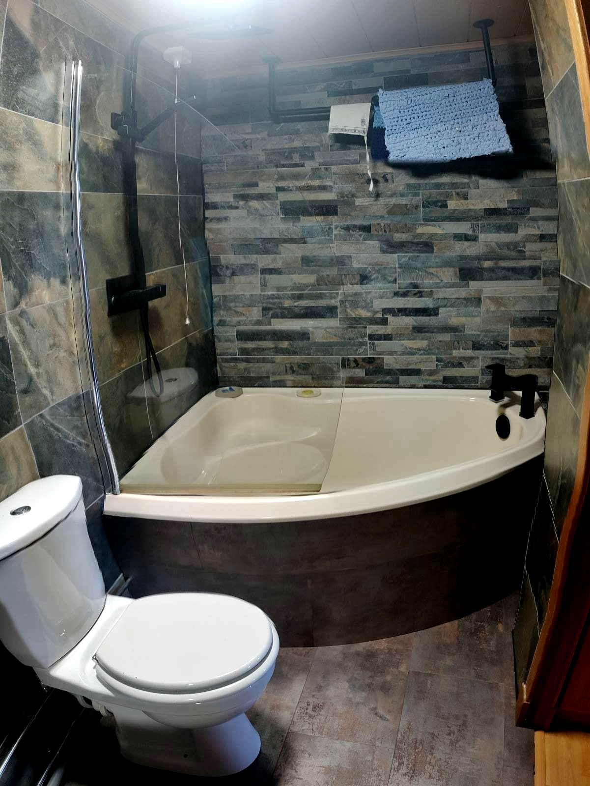 After: Bathroom with stone effect grey an brown tiles, black shower and taps over the corner bath