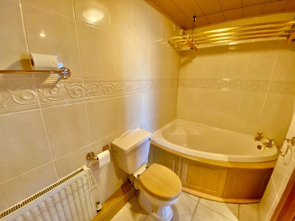 Before: Cream, gold and beech decor in an aging bathroom, showing toilet and corner bath with a pulley clothesline